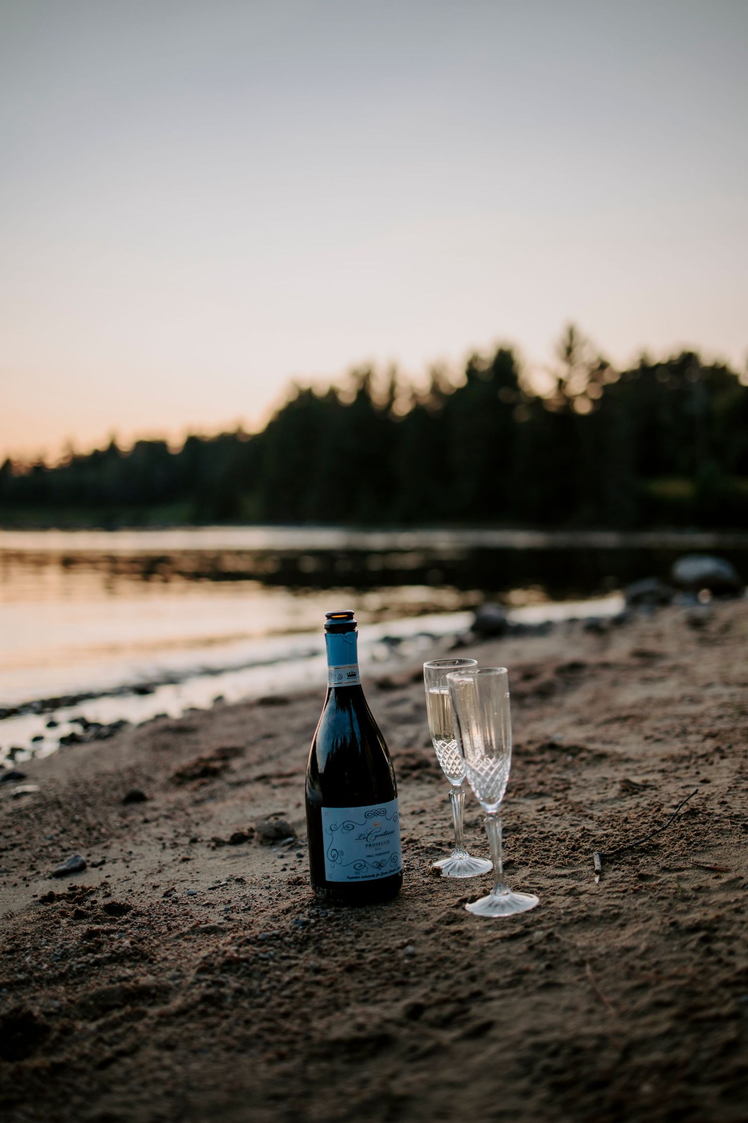 Wine bottle and glasses set up on a beach at sunset.