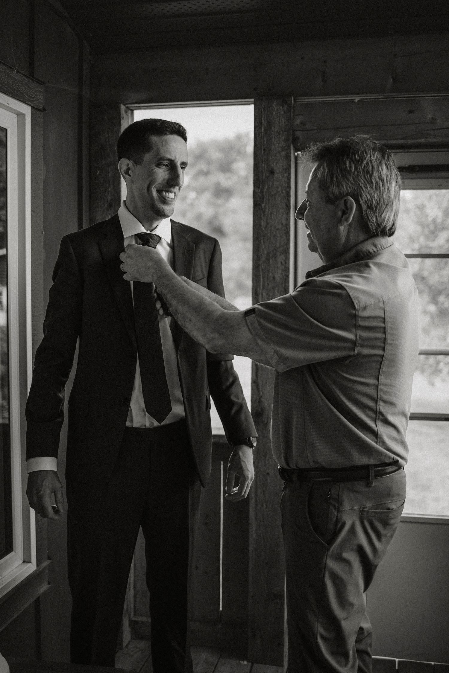 A tie adjustment moment captured in black and white during wedding preparations.