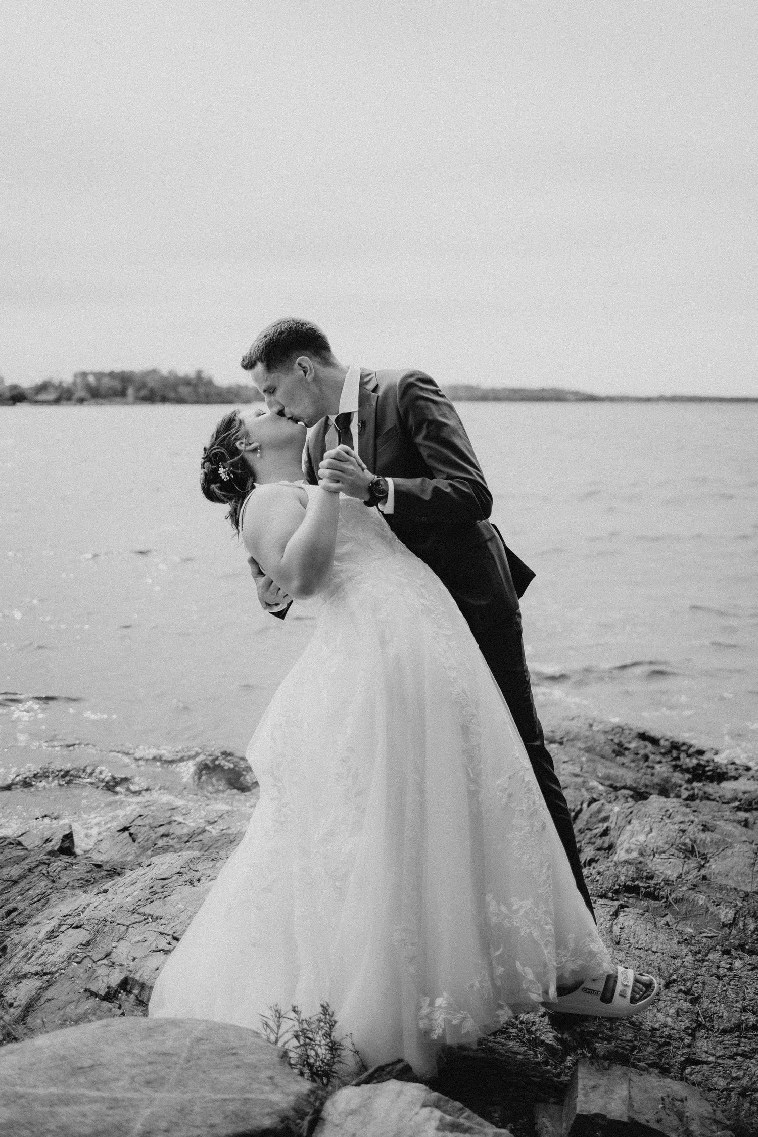 Romantic black and white wedding portrait of couple kissing on rocky shore.