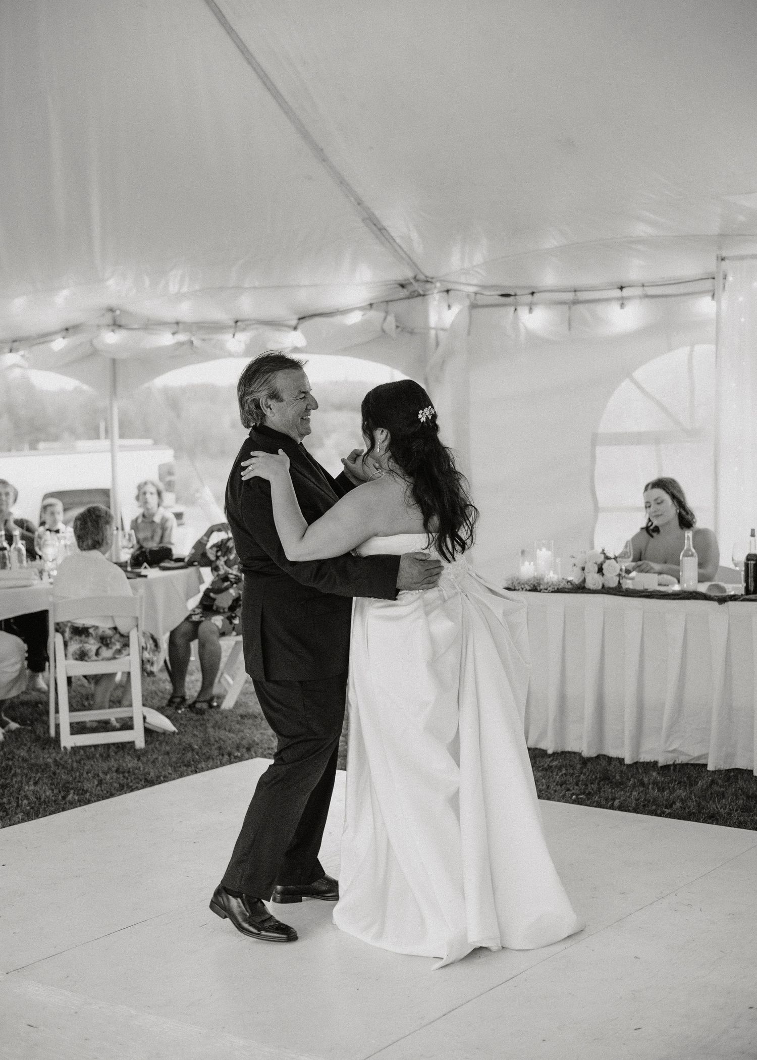 A couple shares their first dance under a white wedding tent at their reception.