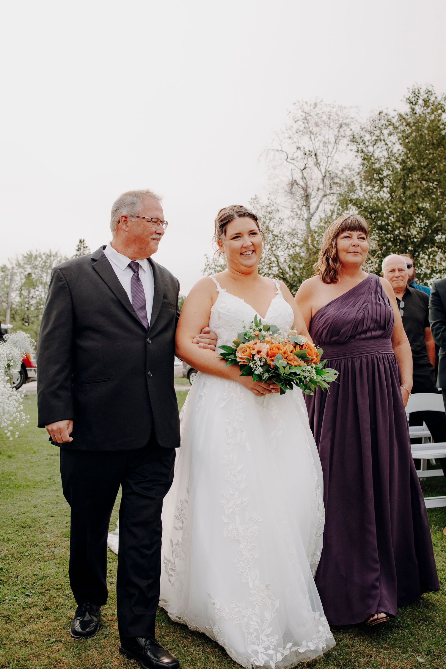 Outdoor wedding ceremony featuring a bride in white with guests in elegant purple attire.