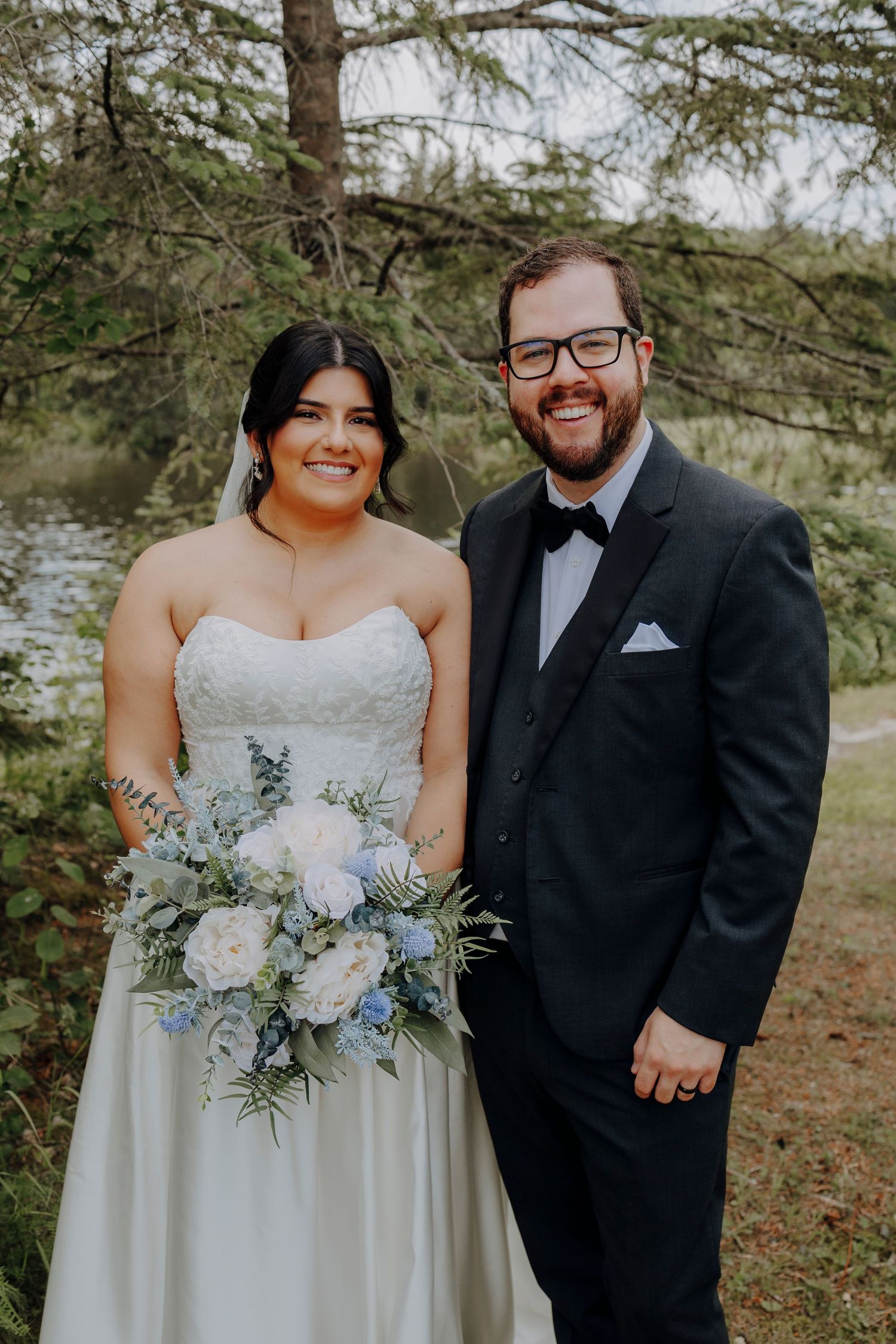 Wedding portrait featuring elegant white bouquet with blue flowers against natural backdrop.