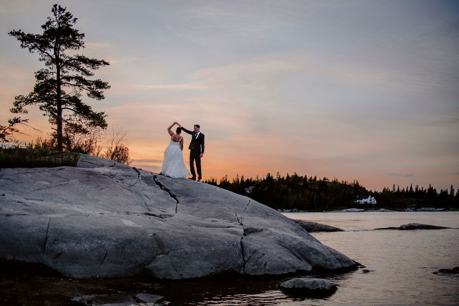 Silhouettes of a wedding couple against a dramatic sunset on rocky coastal cliffs.