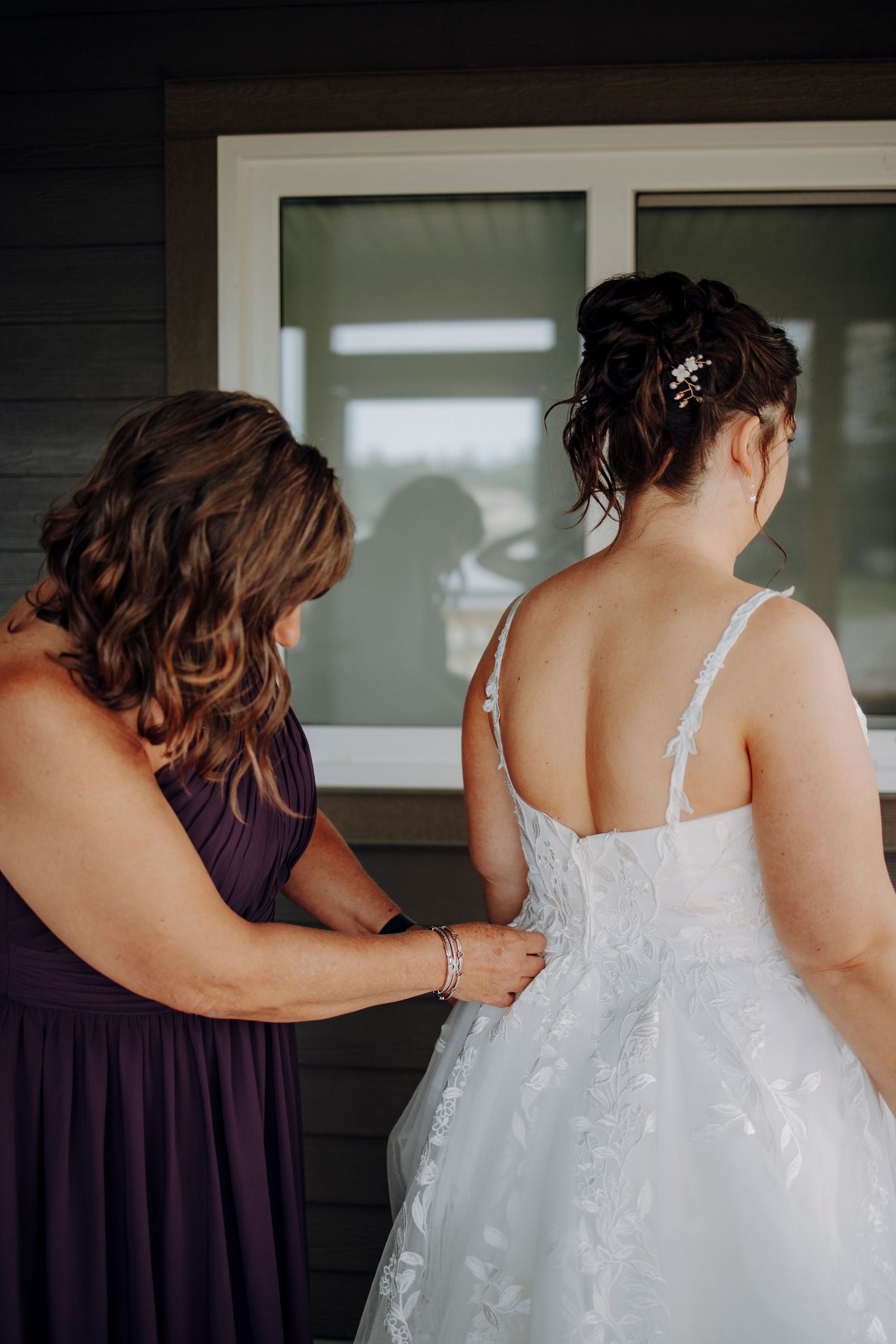 A close-up view of bridesmaids helping with the back of a white wedding dress.