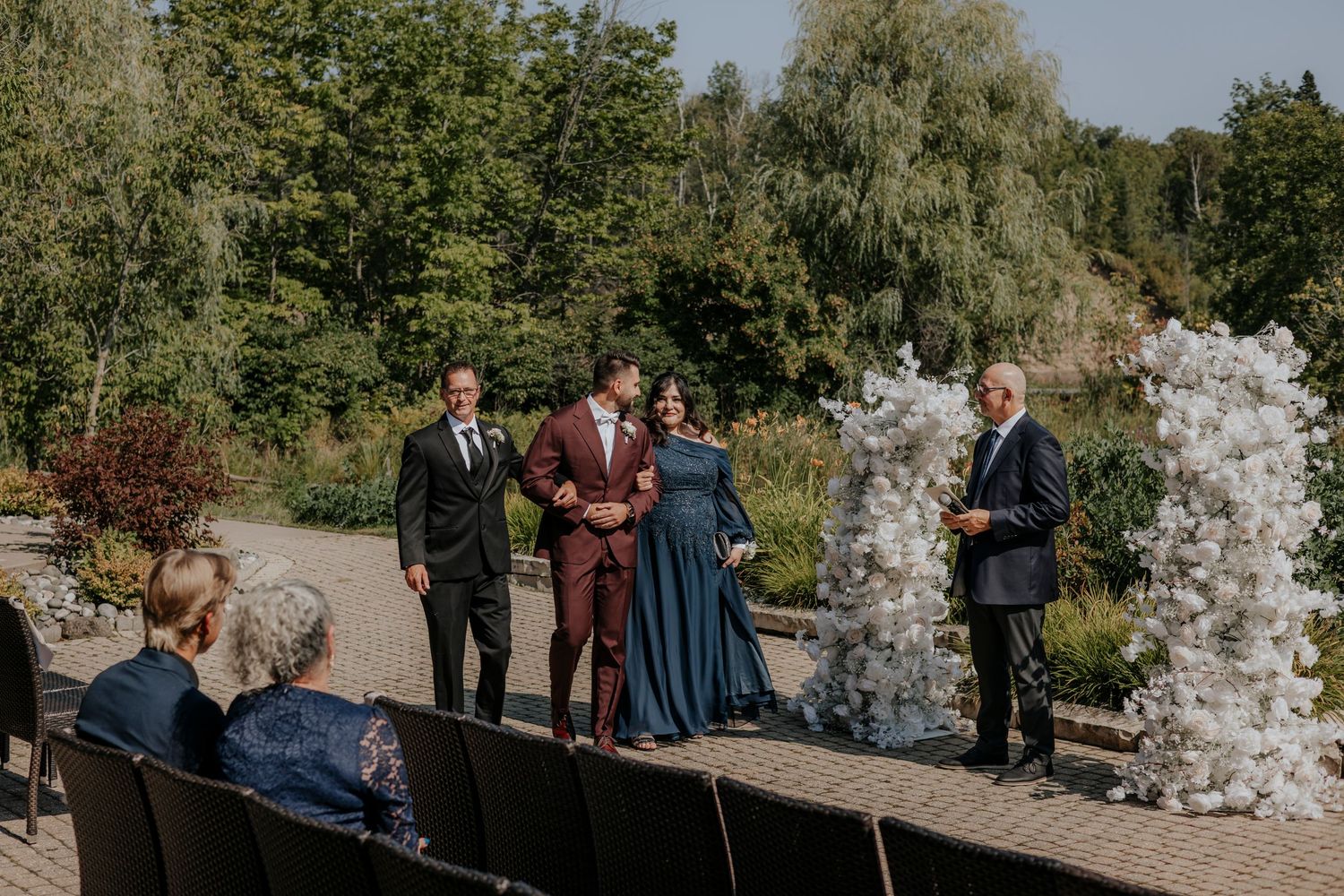 An outdoor wedding ceremony setup with white floral arrangements and guests seated.