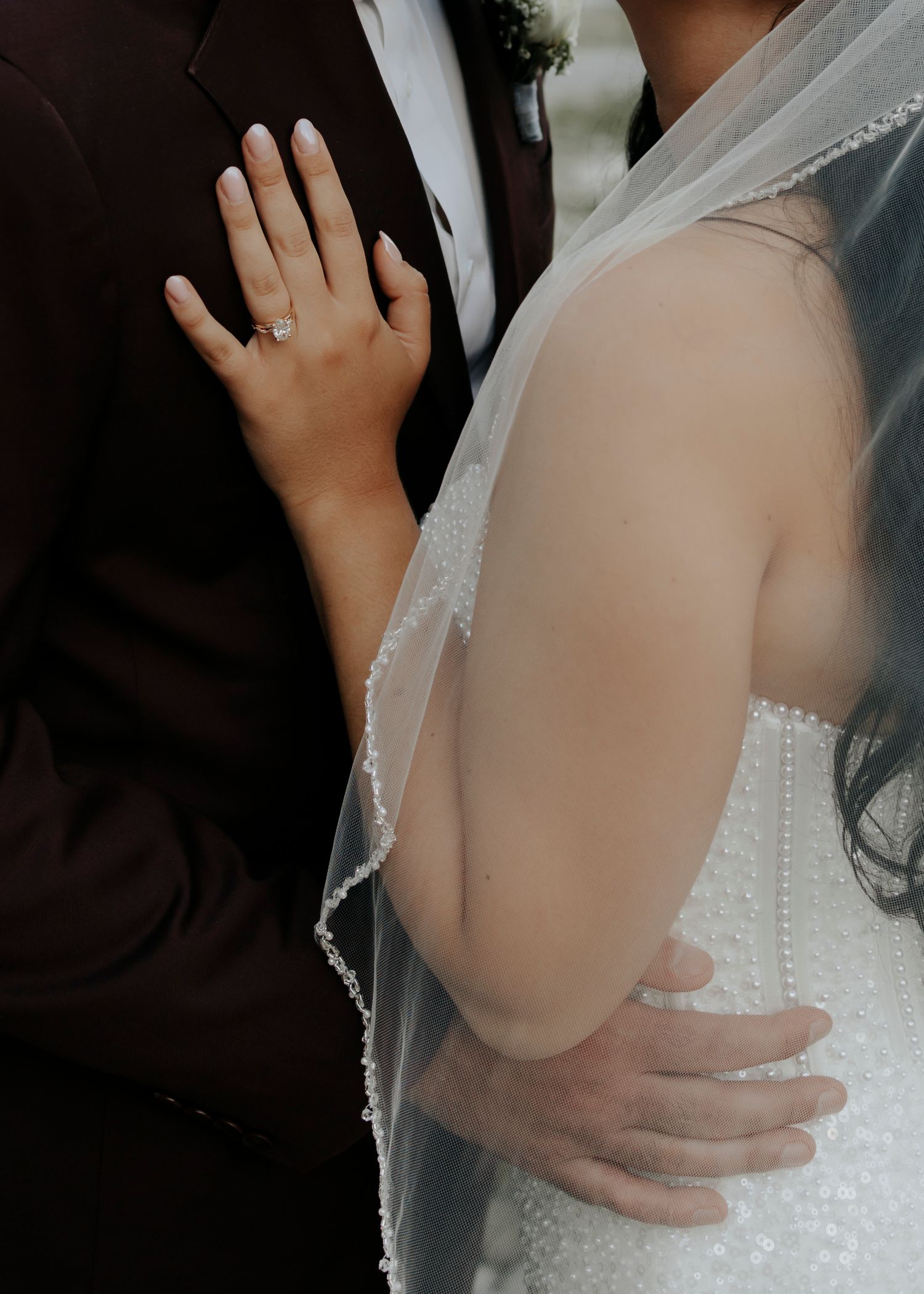 Close-up details of hands adjusting a white wedding dress with delicate lace and veil.