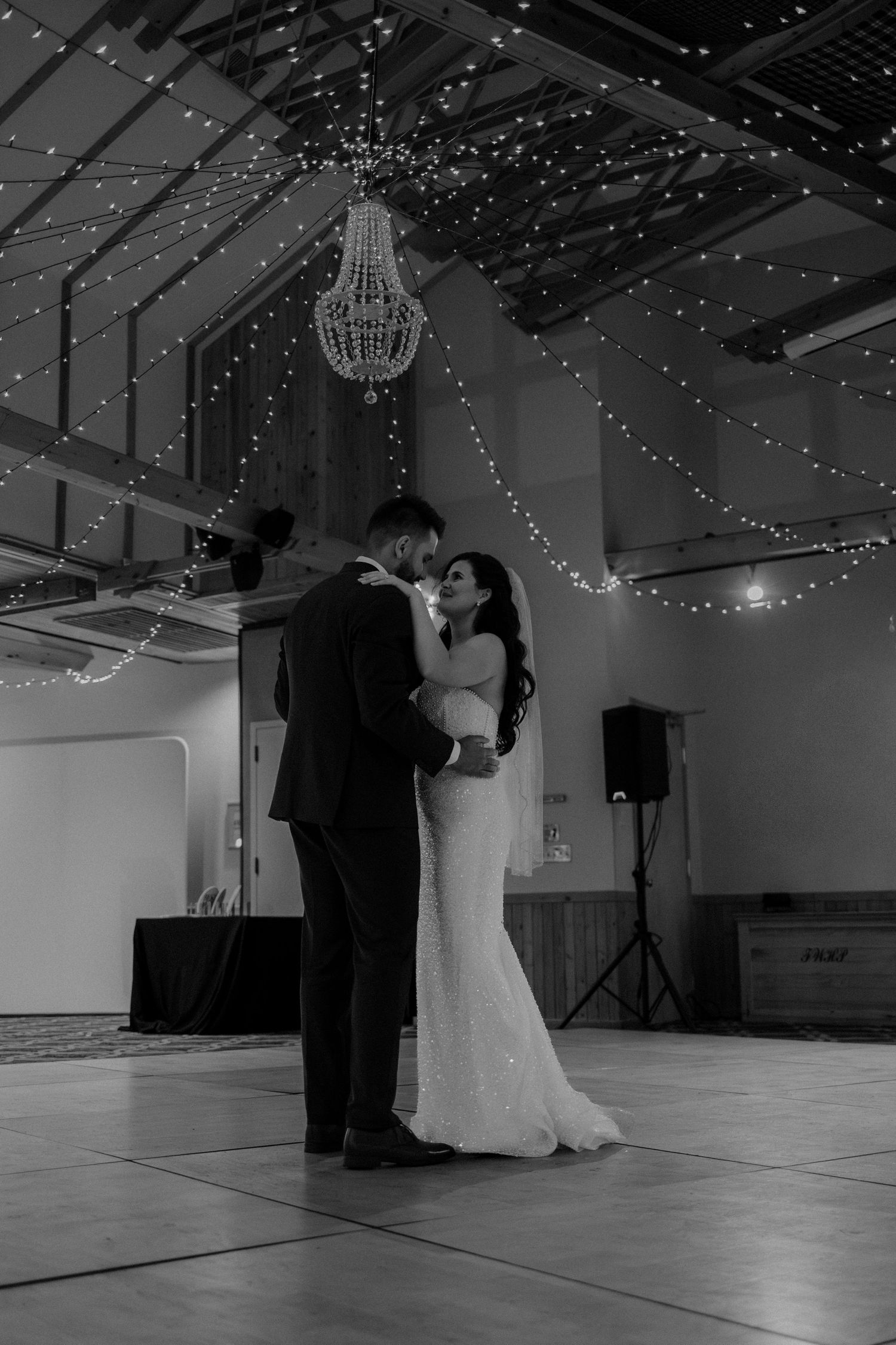 A couple shares their first dance under twinkling lights in a spacious ballroom with high ceilings.