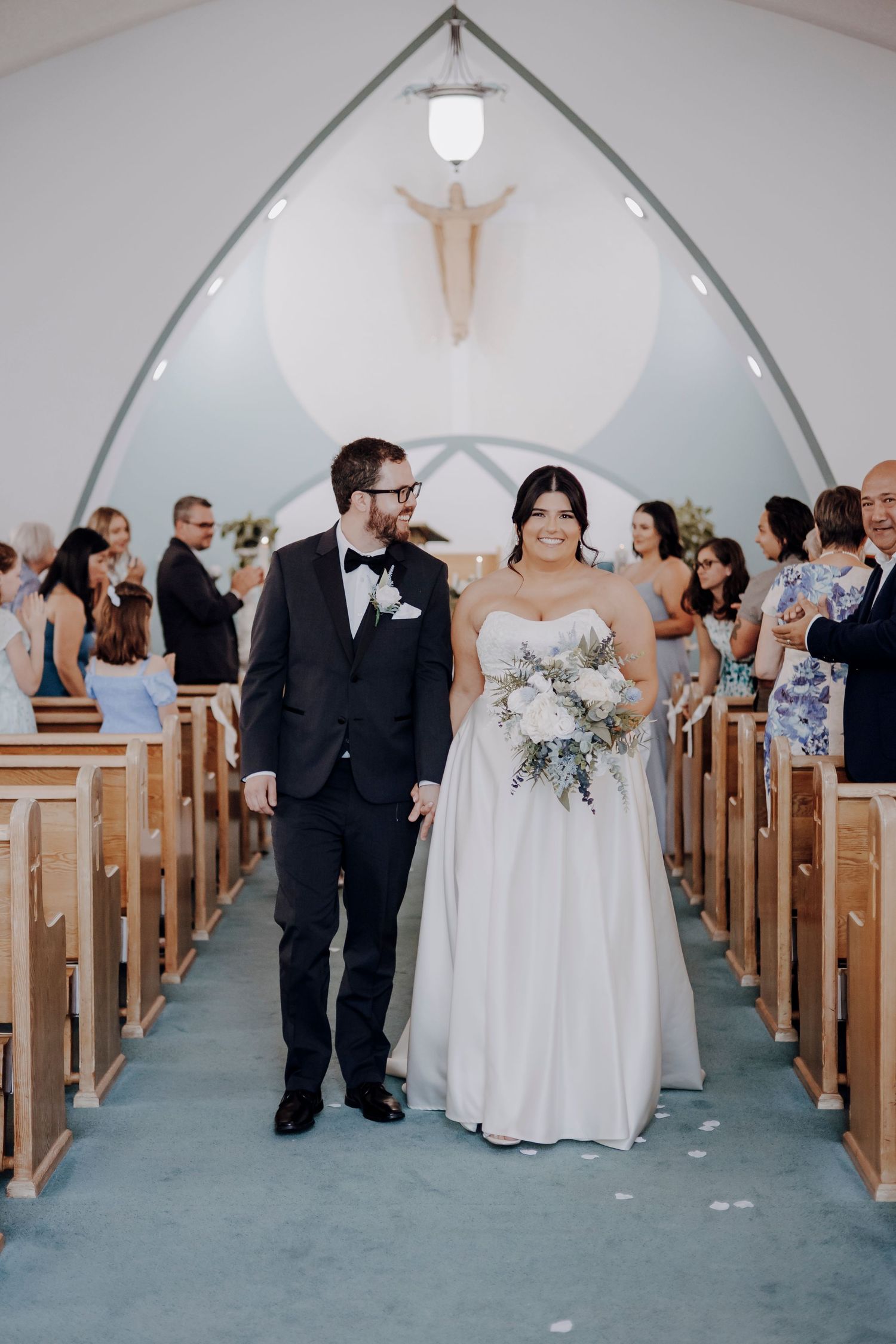 Newlyweds exit church ceremony while guests look on in modern chapel with minimalist decor.
