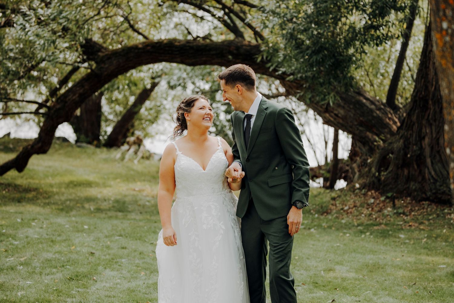 Wedding couple strolling together under large trees in garden setting.