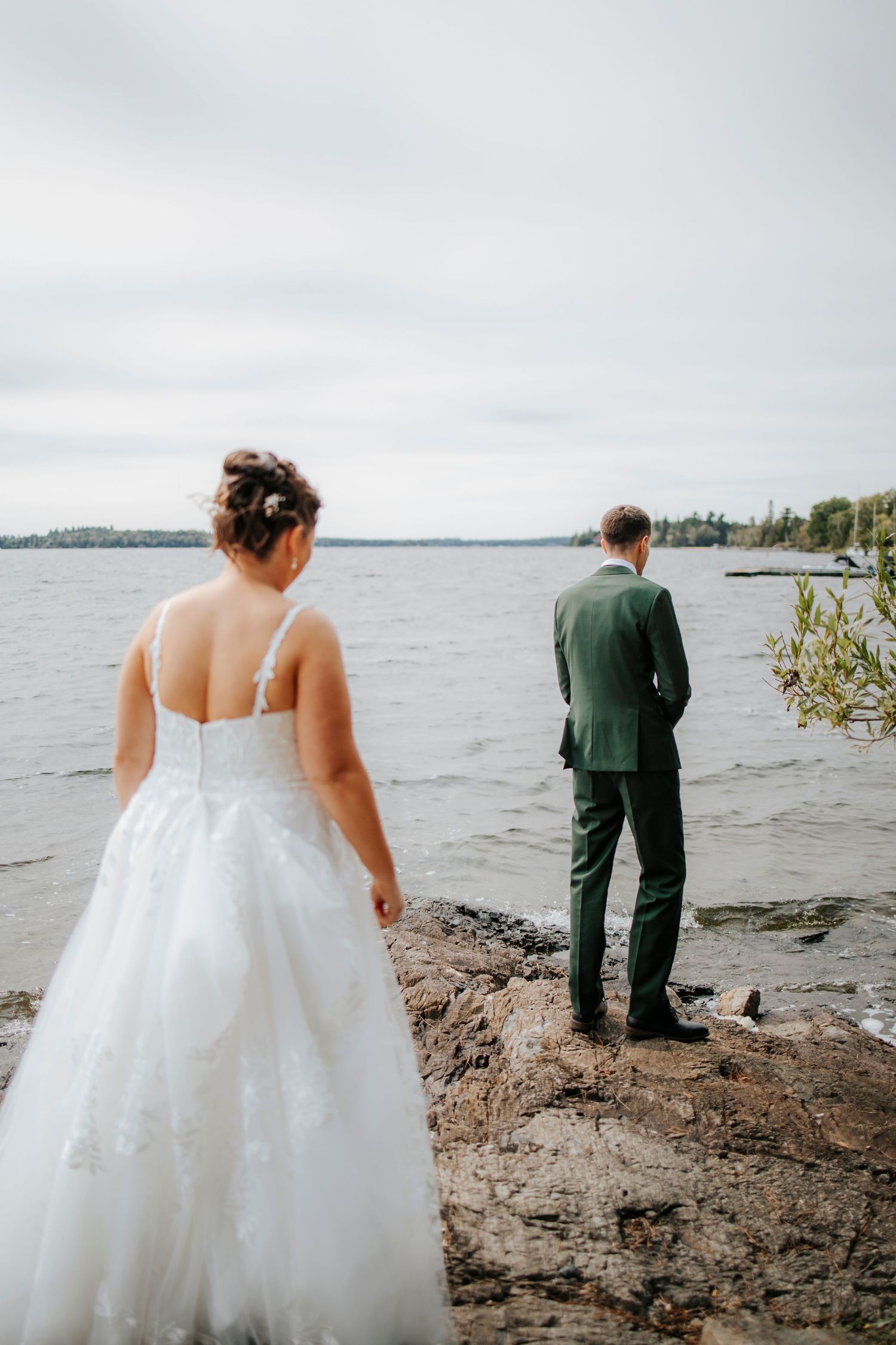 Couple shares private moments along rocky lakeshore during wedding photoshoot.