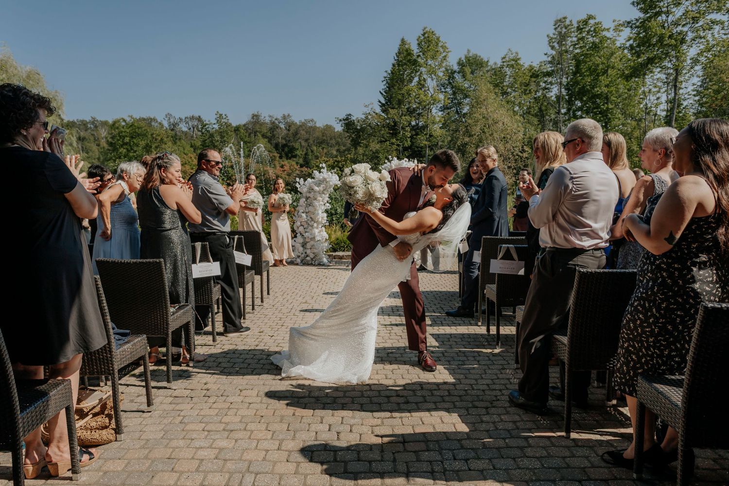 Outdoor wedding ceremony setup with guests seated on chairs under blue sky.