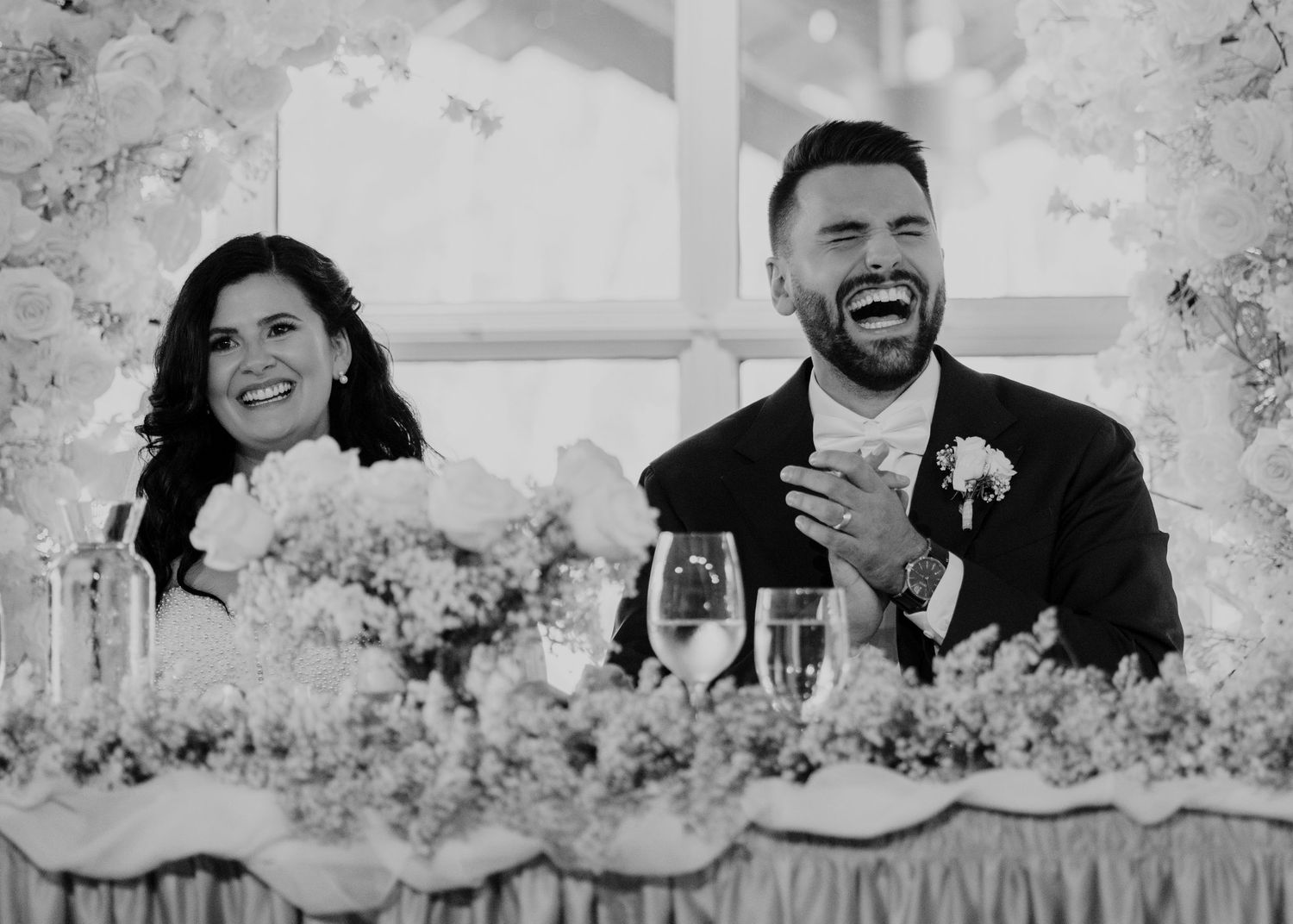Wedding party shares laughs at decorated head table during reception.