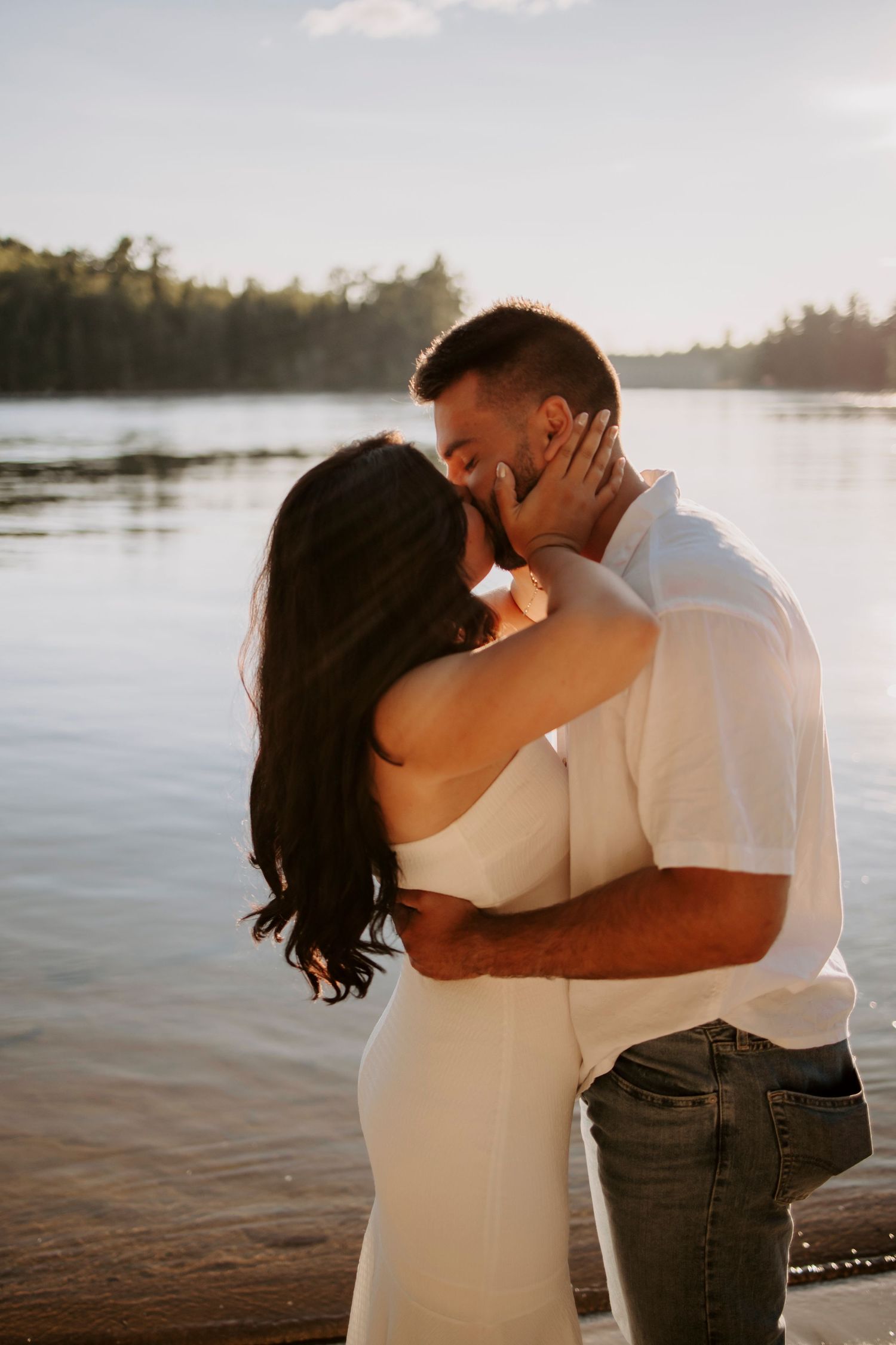 A tender moment between a couple embracing on a lakeside beach at sunset.