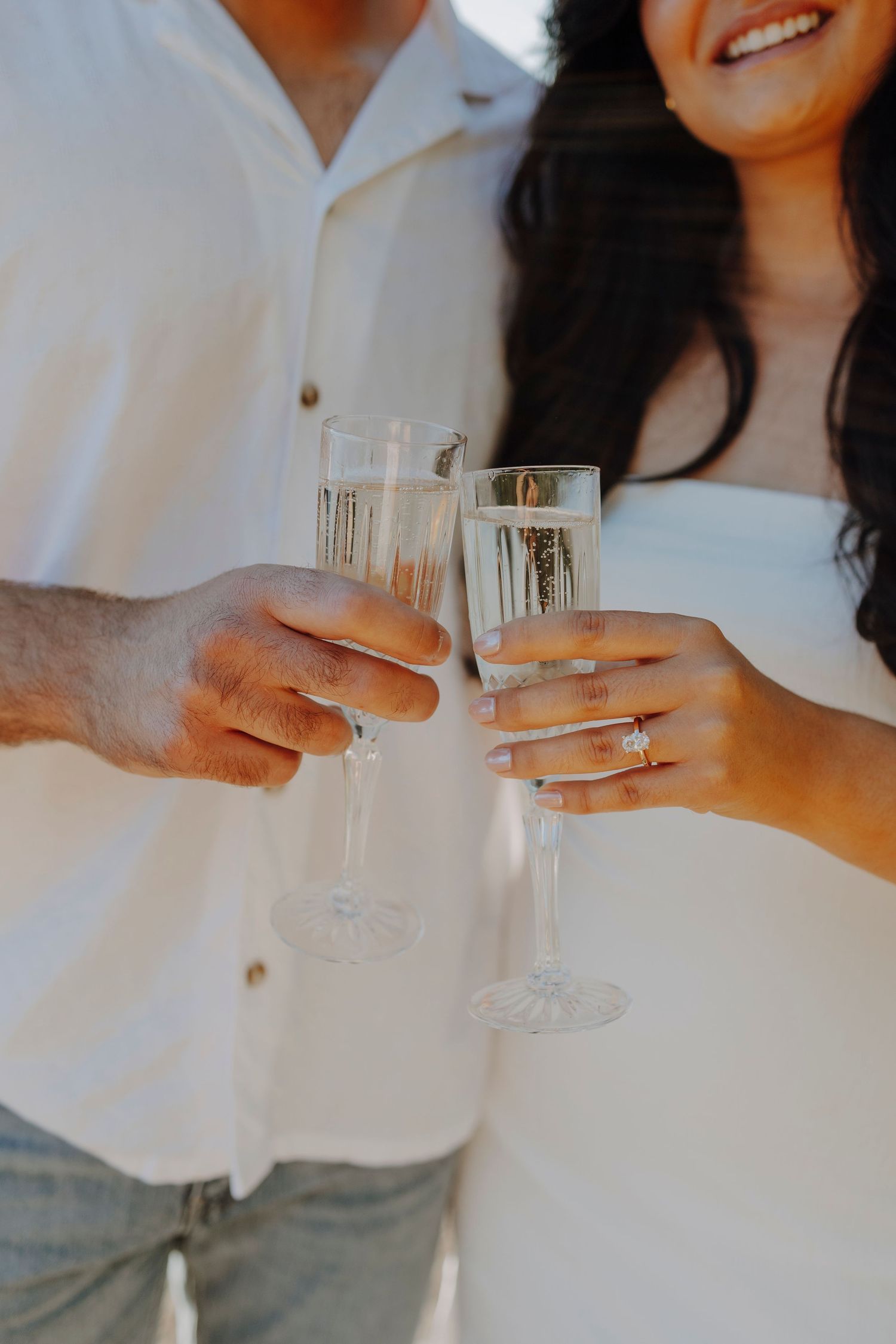 Newly engaged couple toasting with champagne glasses showing off the ring.