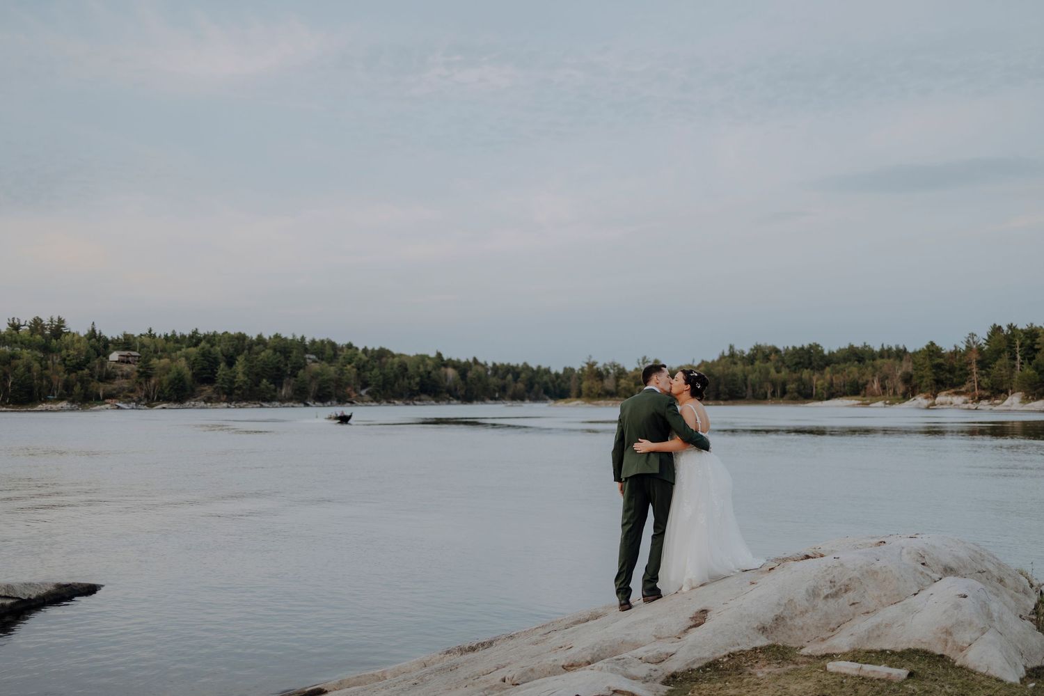 Person standing on rocky shore overlooking serene lake landscape at dusk.