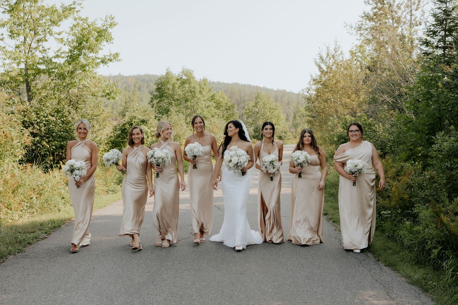 Wedding party walking together on a path surrounded by lush greenery.