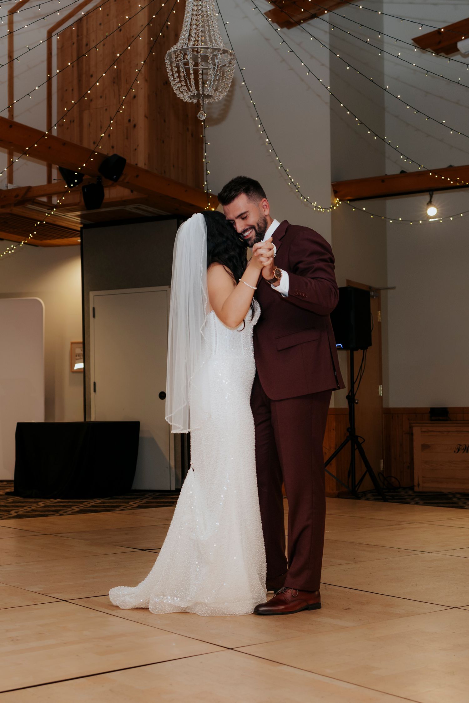 First dance moments under string lights in a rustic wedding venue.