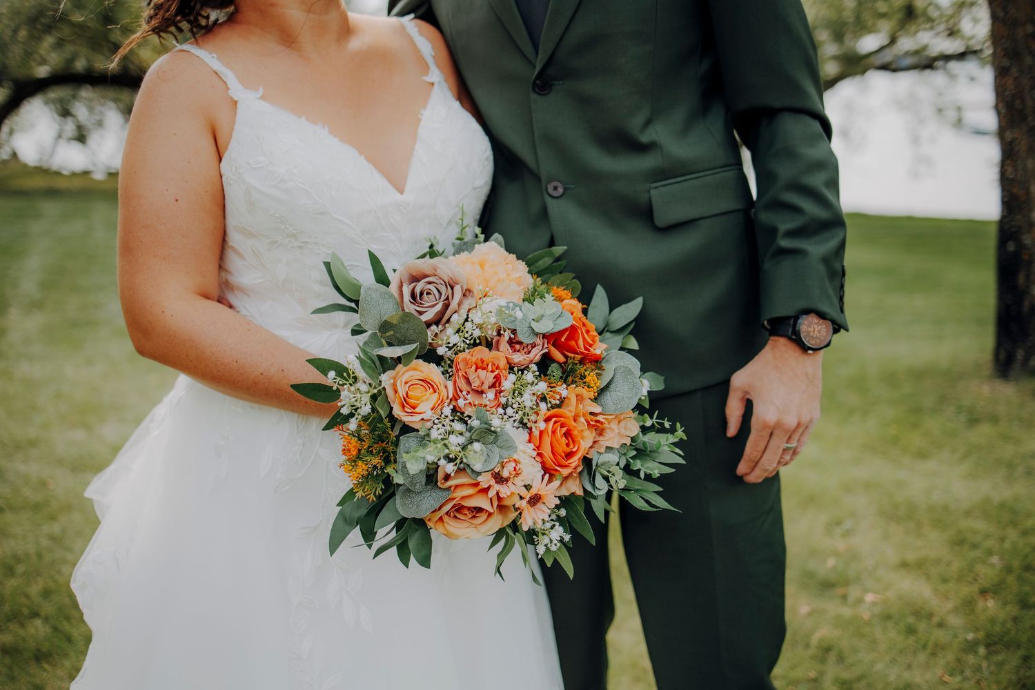 Wedding couple posing outdoors with bride holding orange and green floral bouquet.