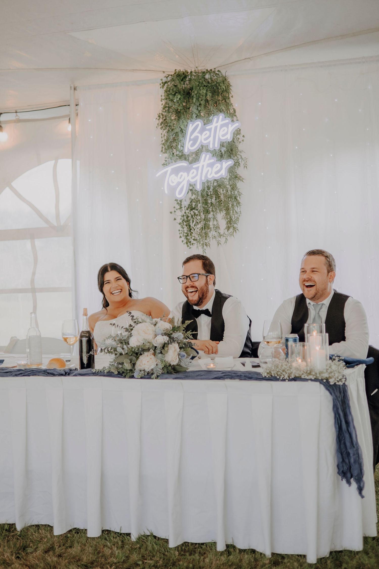 Wedding reception head table decorated in white linens with hanging greenery.