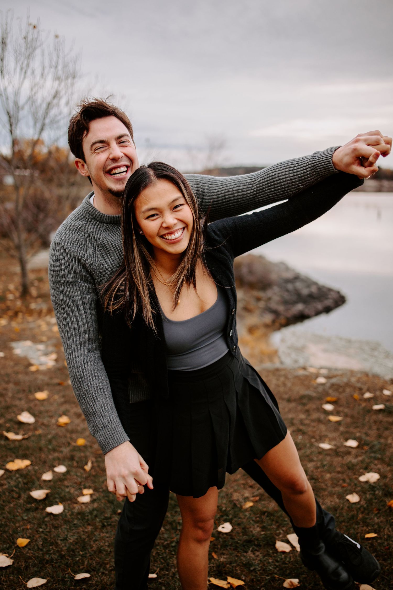 A joyful couple poses together during an autumn photoshoot by a scenic lake.