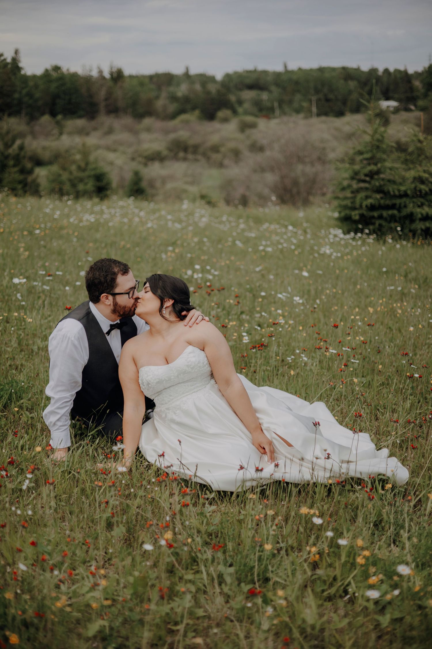 A romantic couple lying together in a wildflower meadow with white daisies and red poppies on their wedding day.
