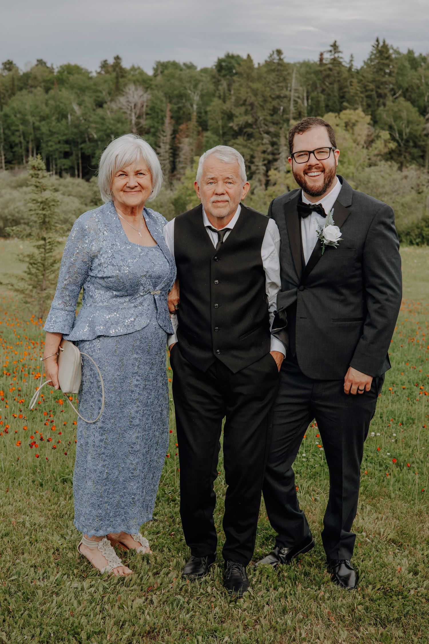 Wedding party members pose together in formal attire against a scenic natural backdrop.