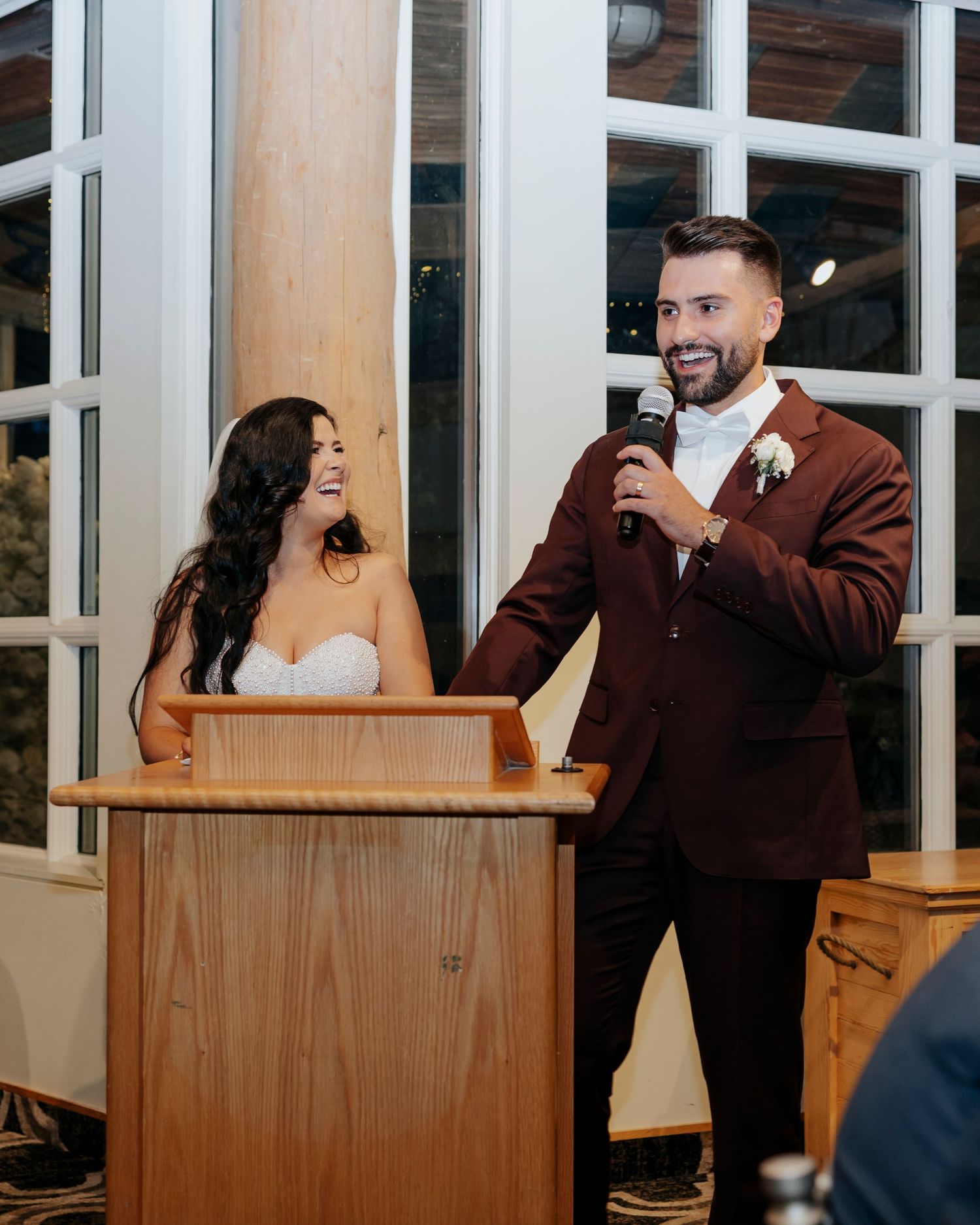 A couple sharing a lighthearted moment while speaking at a wooden podium.