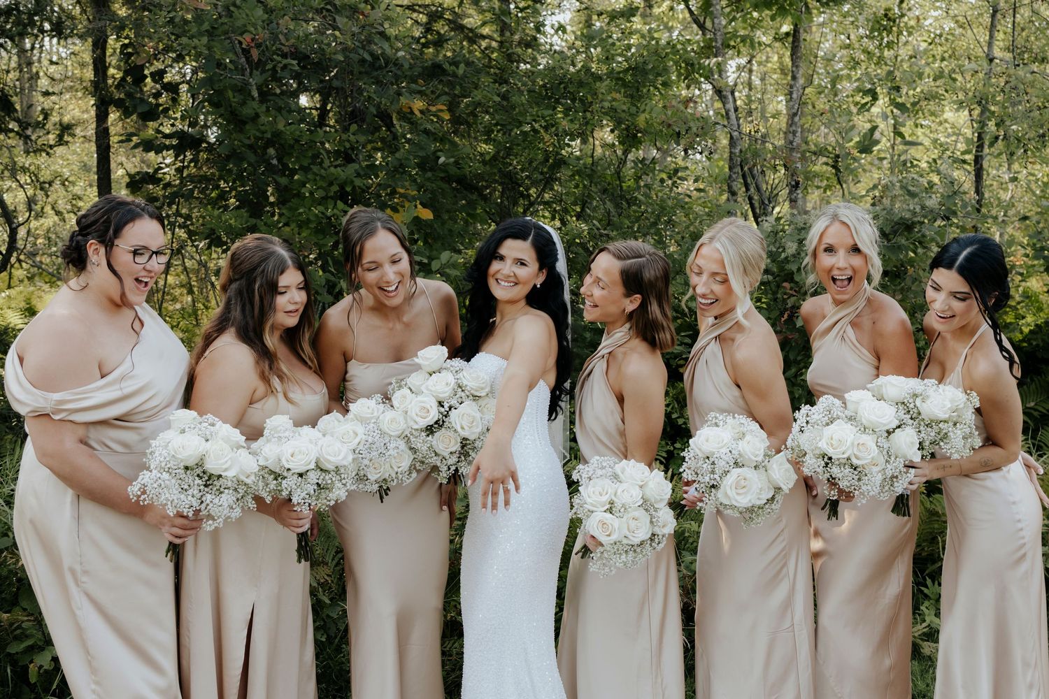 Bridesmaids in champagne dresses holding white bouquets pose outdoors.