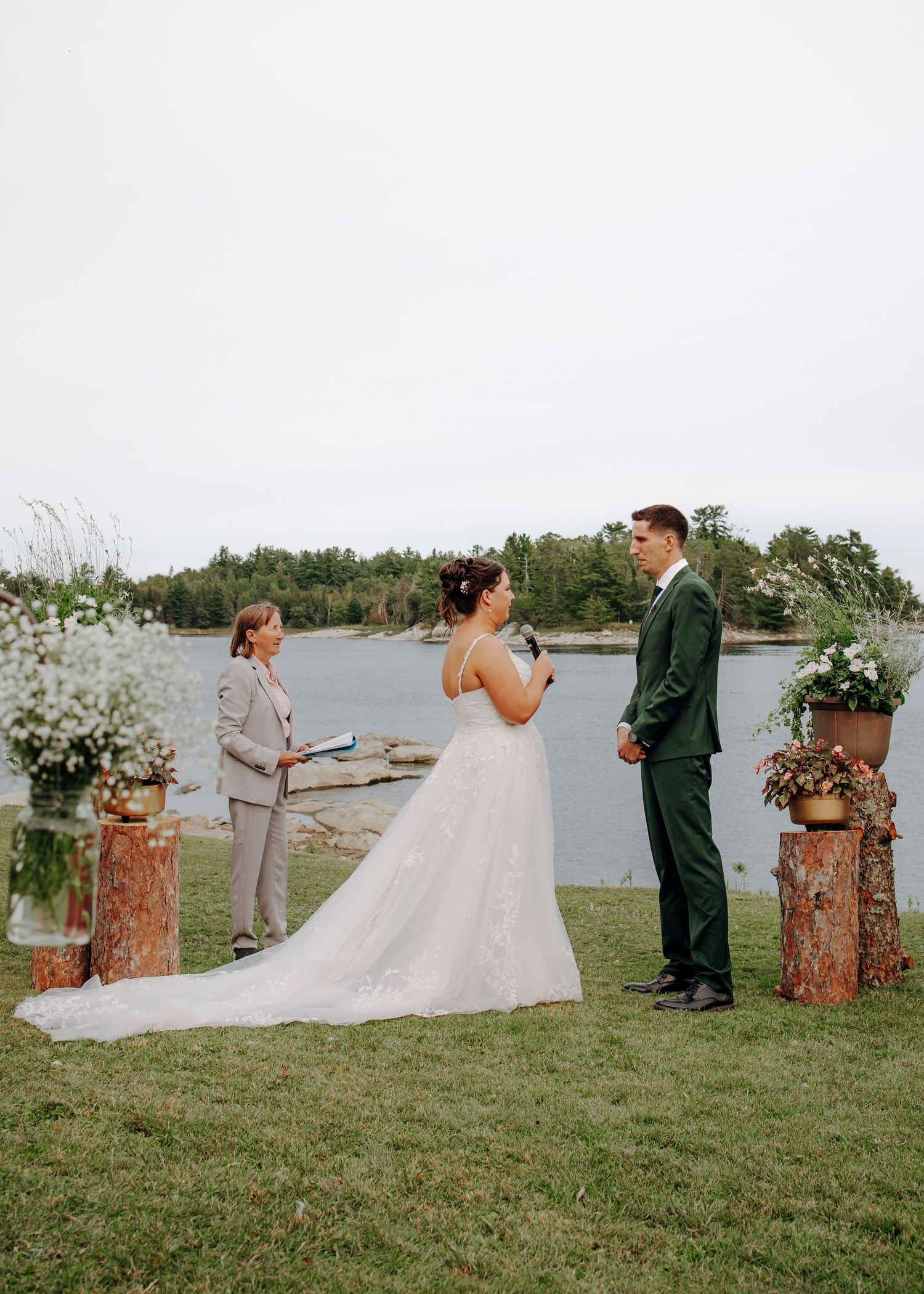 Wedding ceremony setup by a lake with wooden stumps and floral arrangements along the aisle.