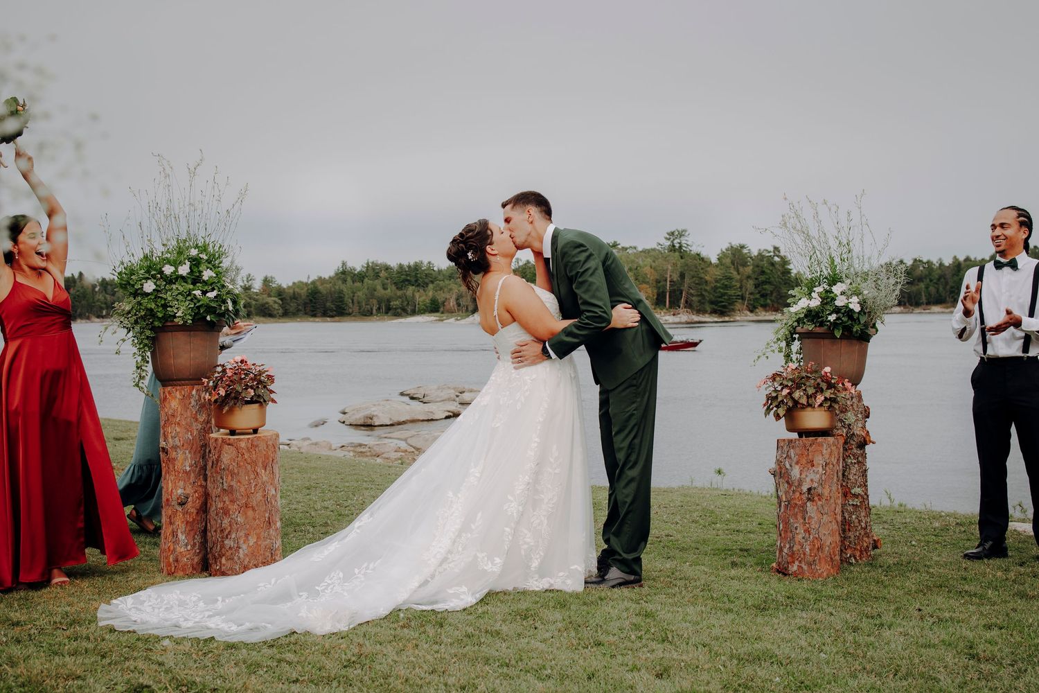 Outdoor wedding ceremony setup with rustic log posts and floral decorations by the water.