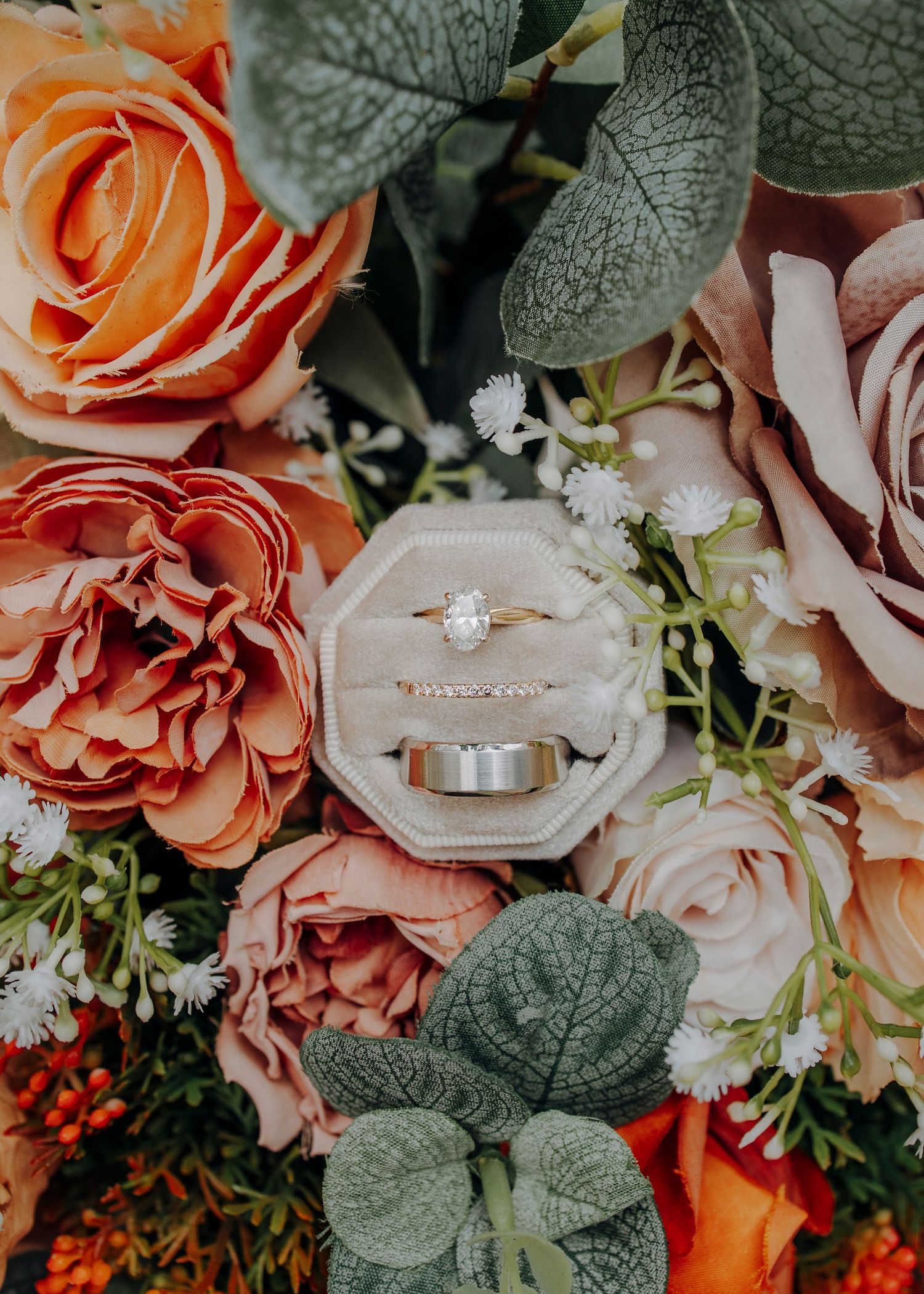 Wedding rings nestled in a velvet box surrounded by coral and peach roses with eucalyptus leaves.