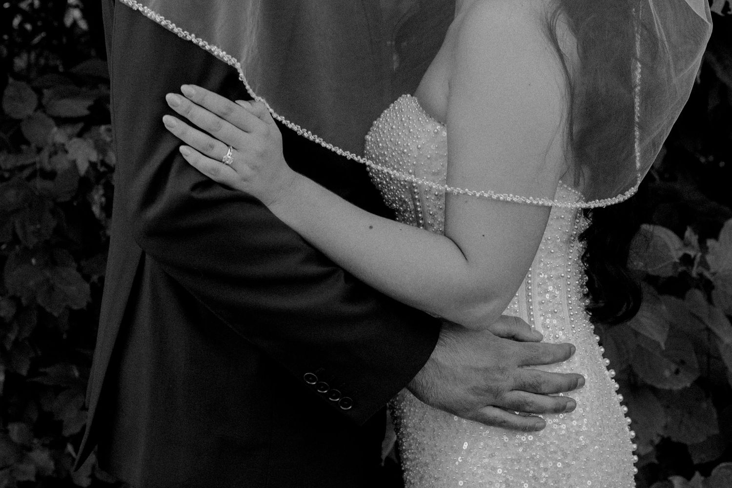 Black and white intimate photo of newlyweds embracing, showing detailed beaded dress and veil.