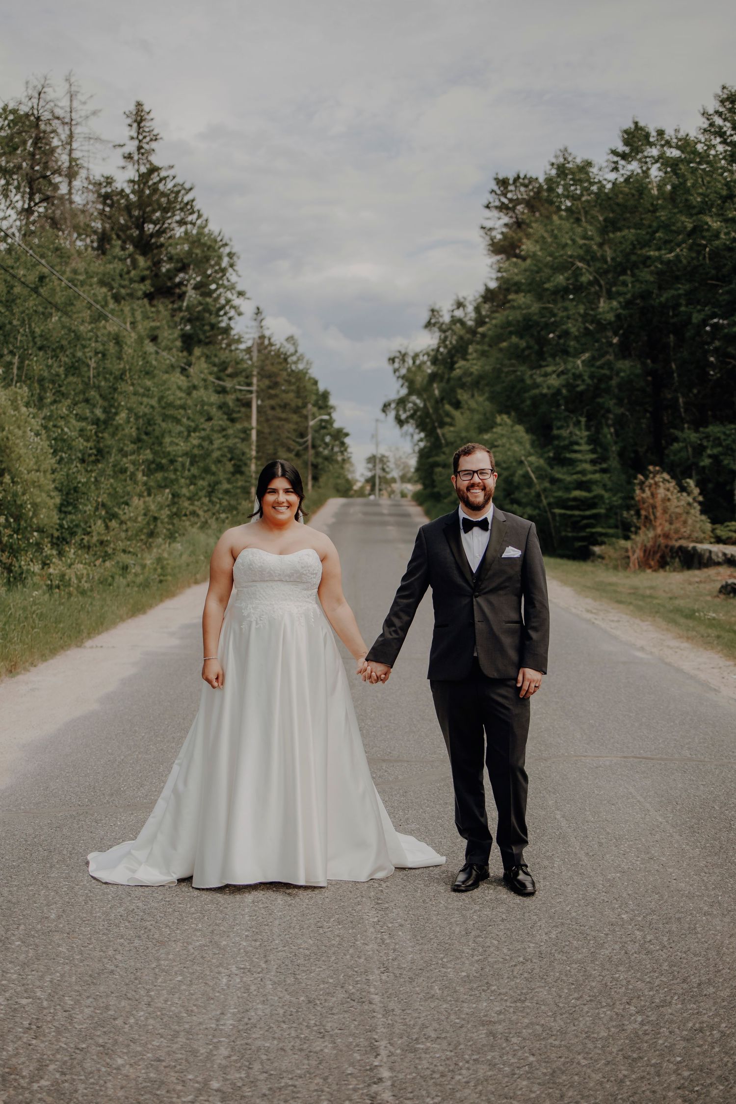 Wedding couple walking together on a rural road surrounded by trees and greenery.