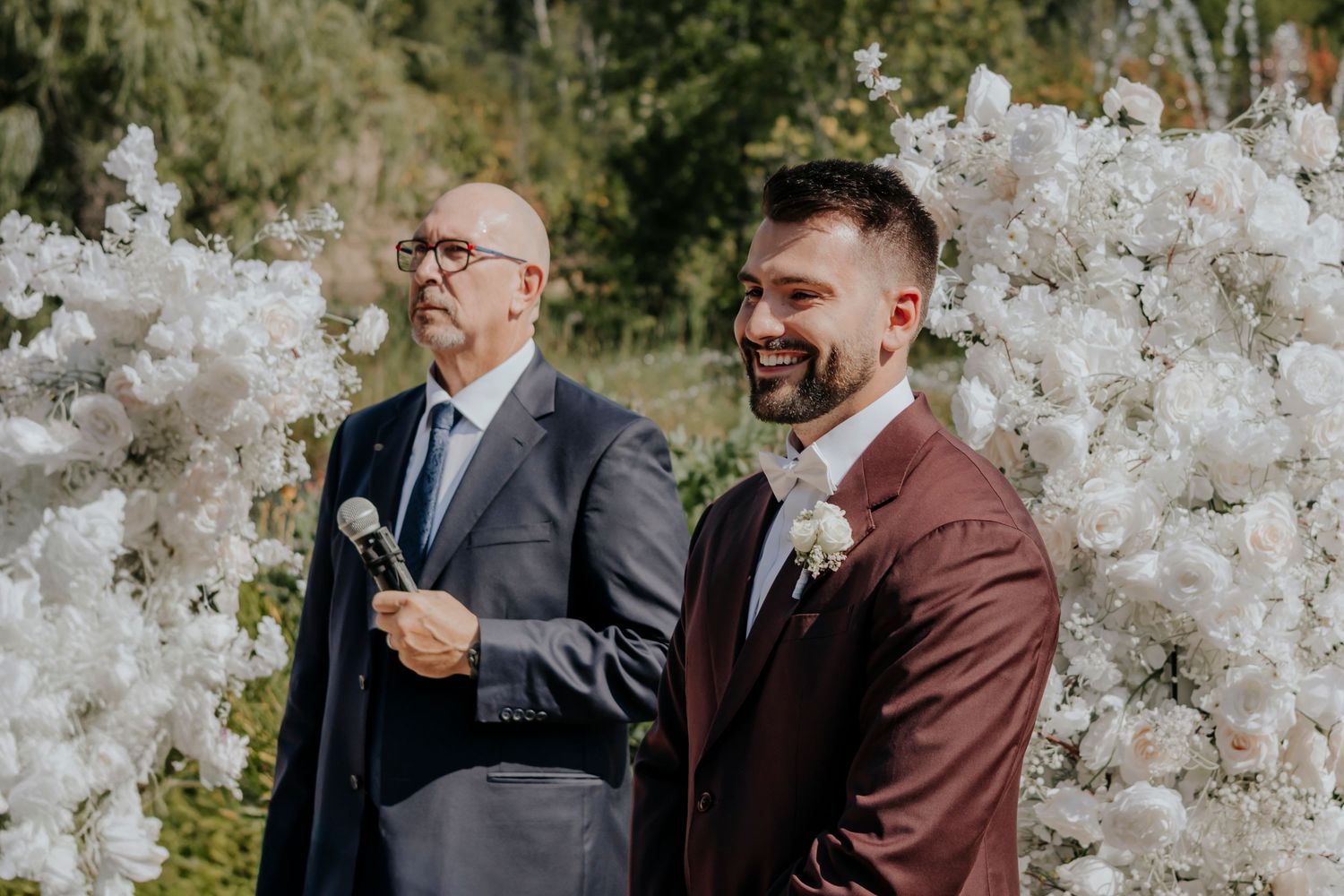Wedding party members sharing laughs and hugs in outdoor setting.