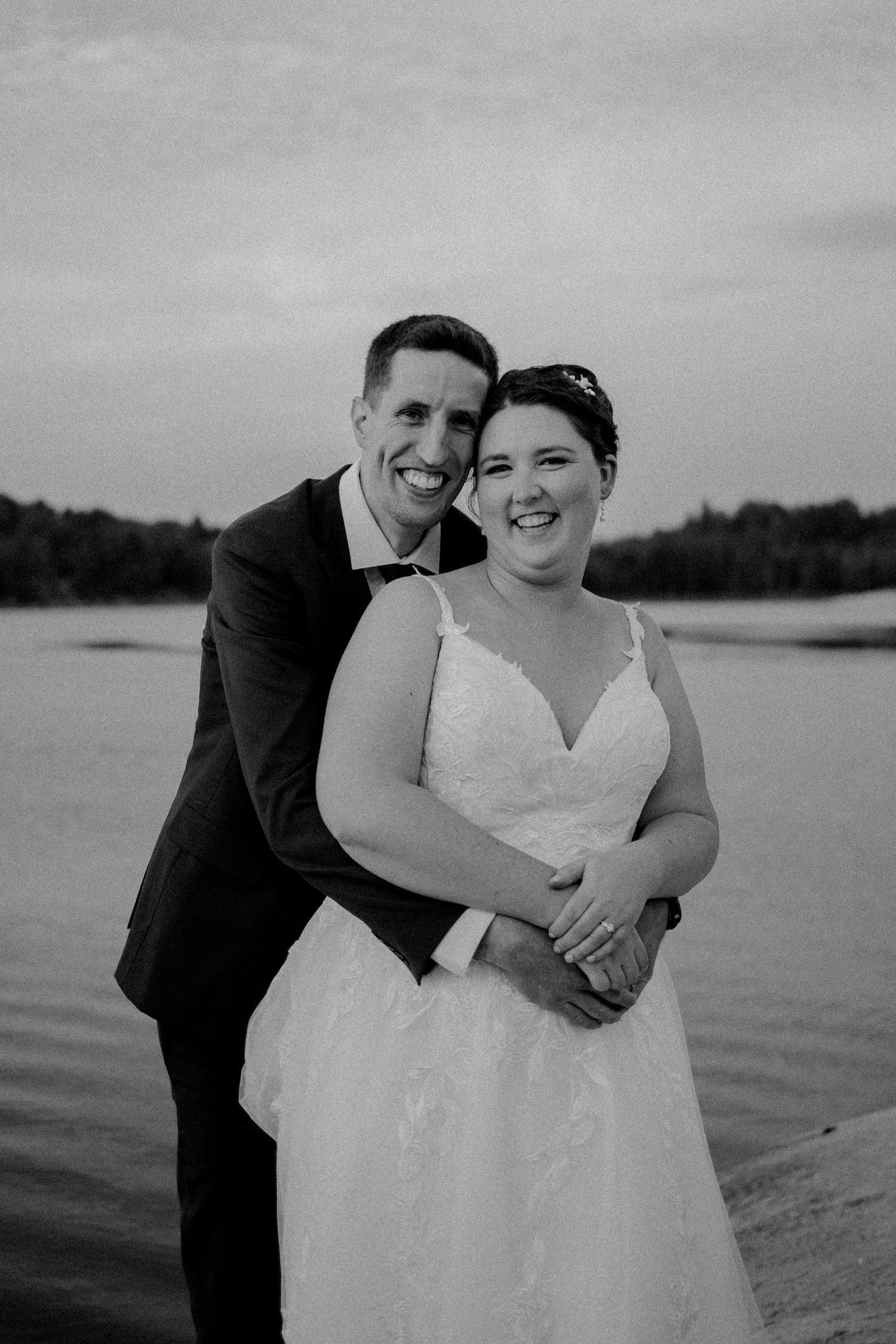 Black and white wedding photos showing joyful moments between newlyweds by a waterfront.