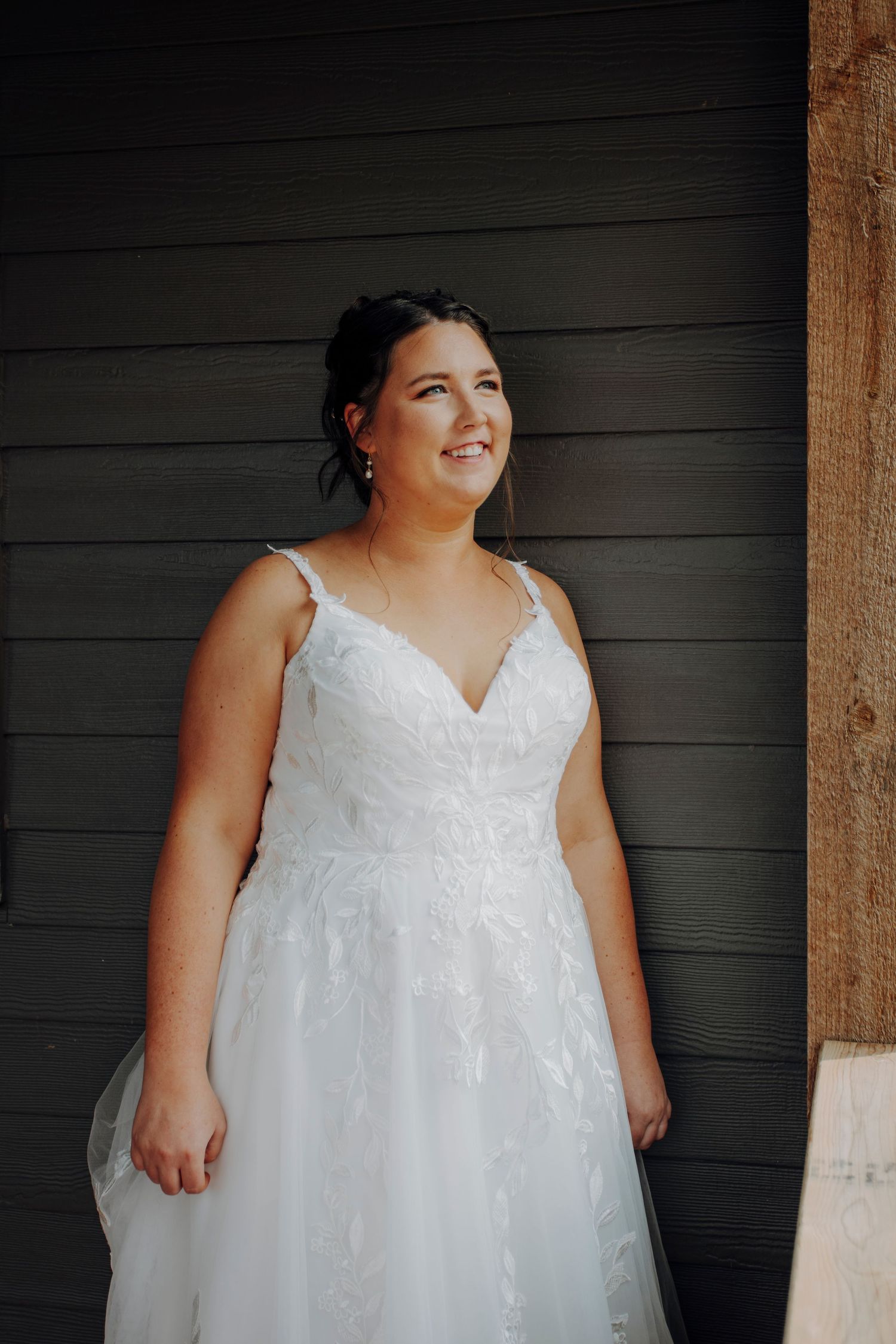 A white lace wedding dress with a v-neckline is displayed against a dark wooden wall.