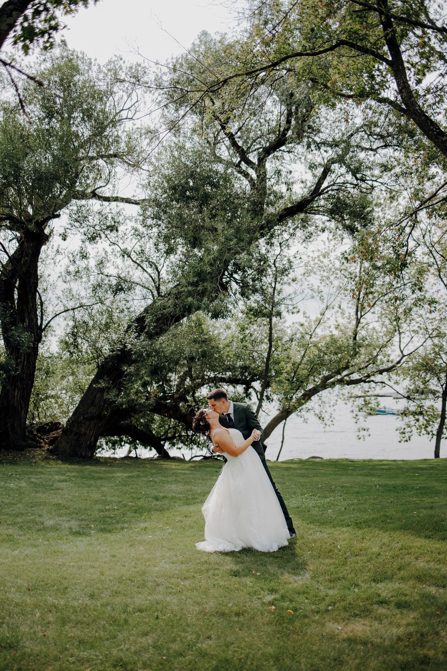 A wedding couple shares intimate moments under tree canopies in a lush green setting.