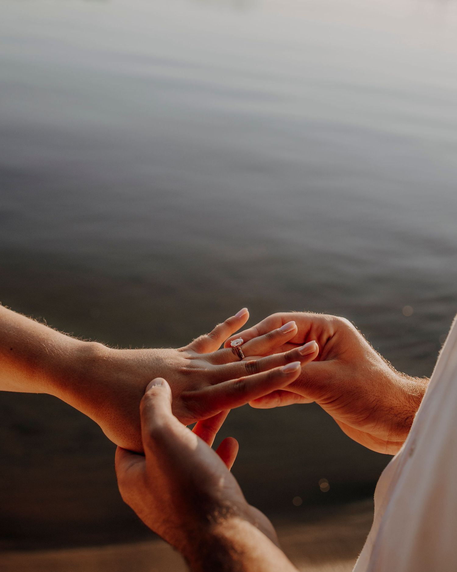 Hands exchanging a ring during sunset by the water.