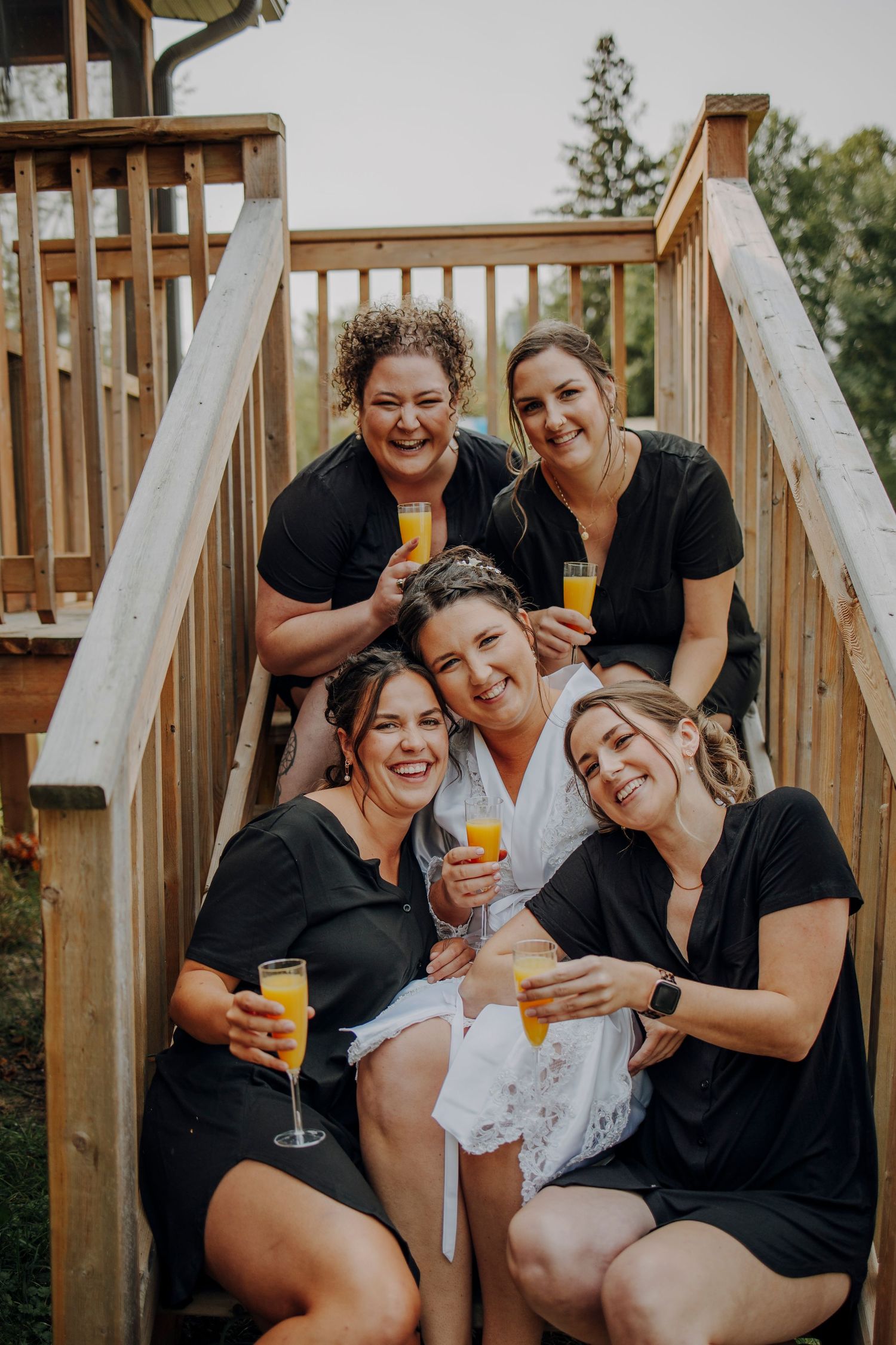 A group in black robes and one in white sharing drinks and laughs together on a wooden deck.