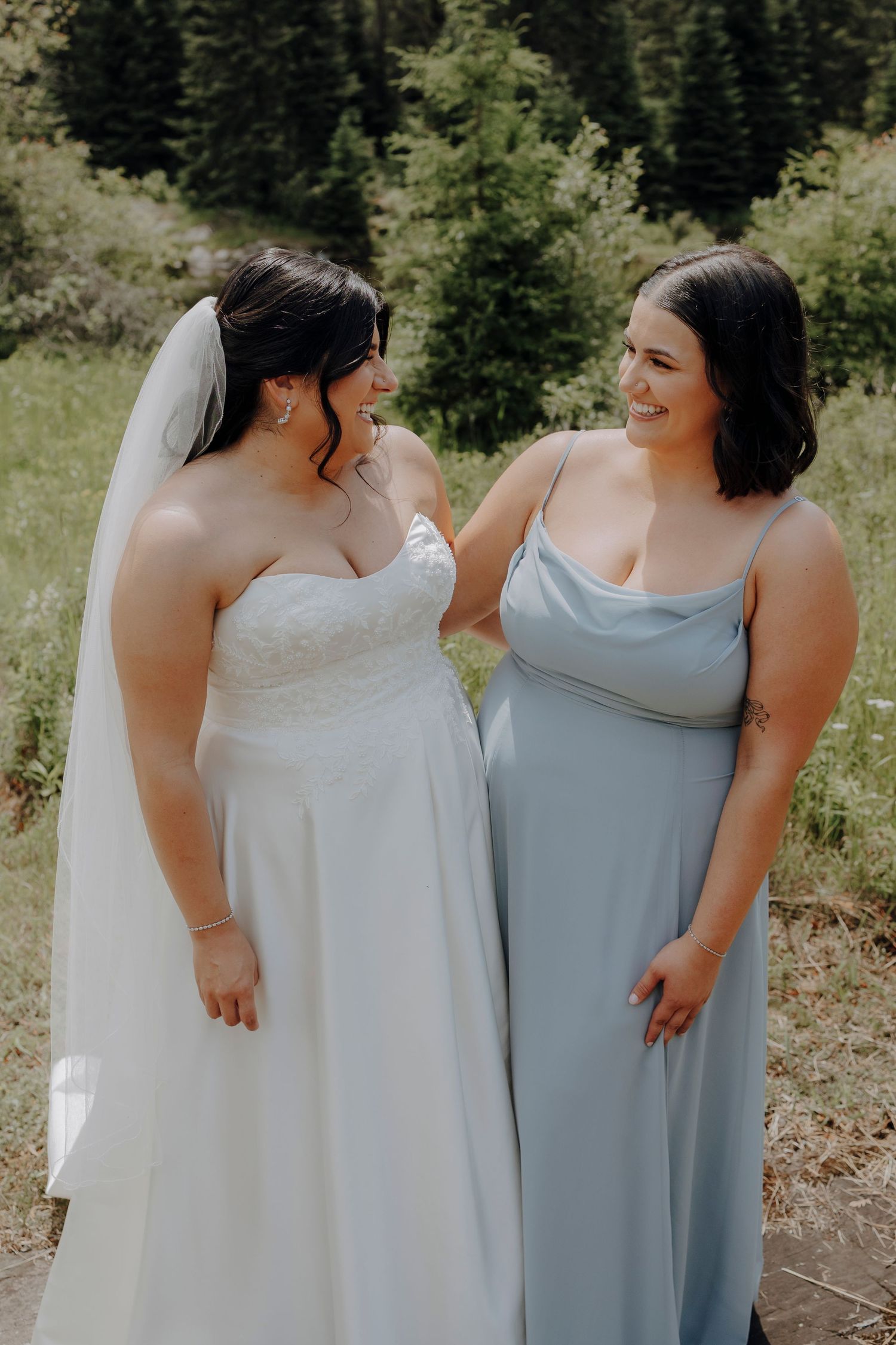 Bridesmaids in light blue and white dresses share candid moments against a mountain forest backdrop.