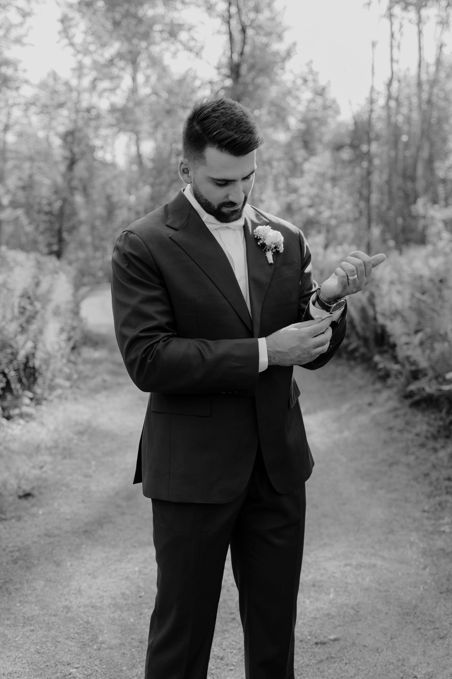 Black and white photo of groomsmen checking their phones on a wooded path.