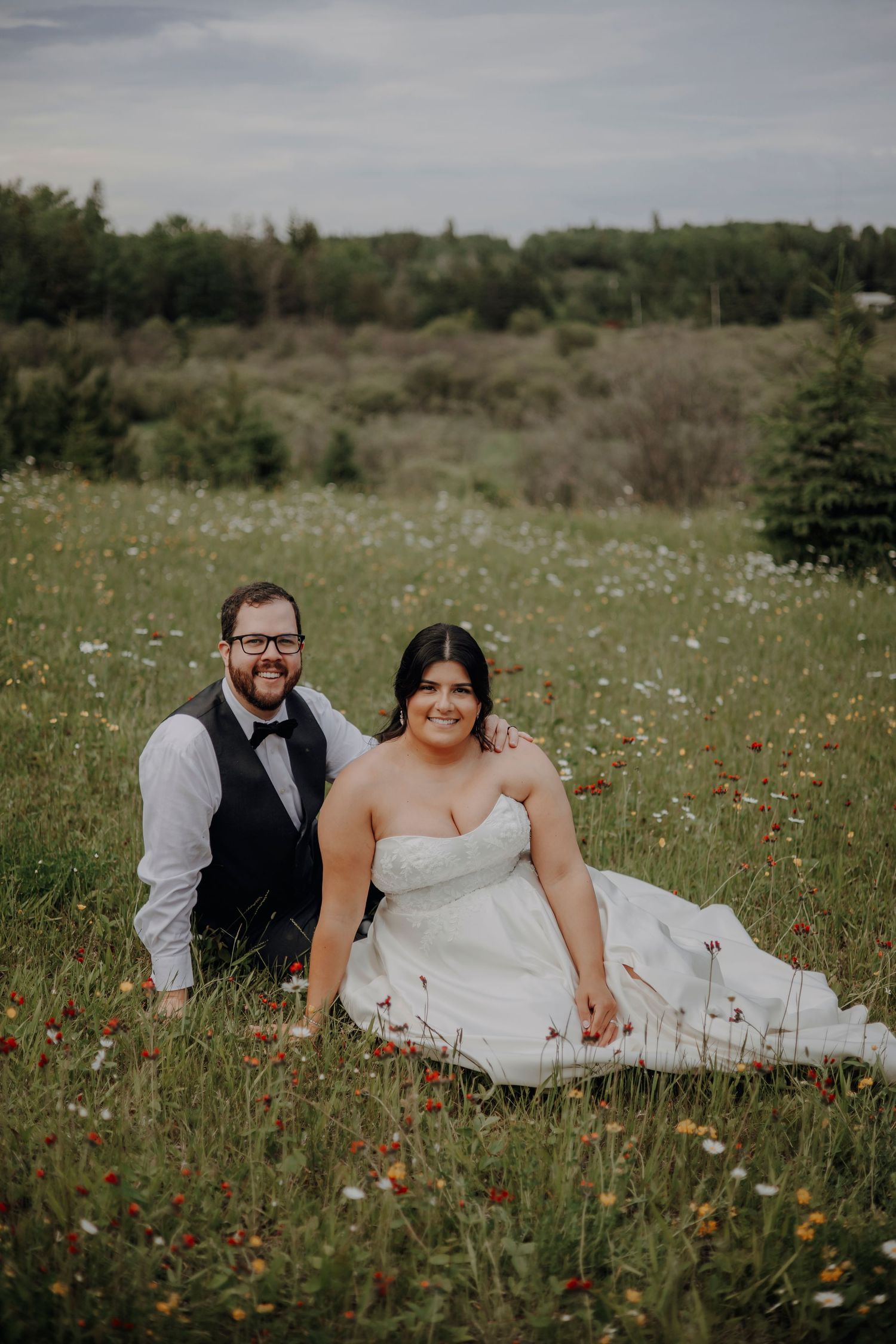 A couple relaxes together in a wildflower meadow filled with daisies and orange blooms on their wedding day.