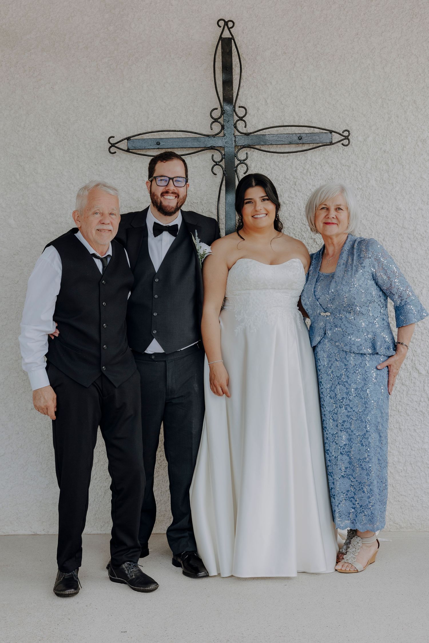 Wedding party poses together against a light gray wall with decorative cross artwork.