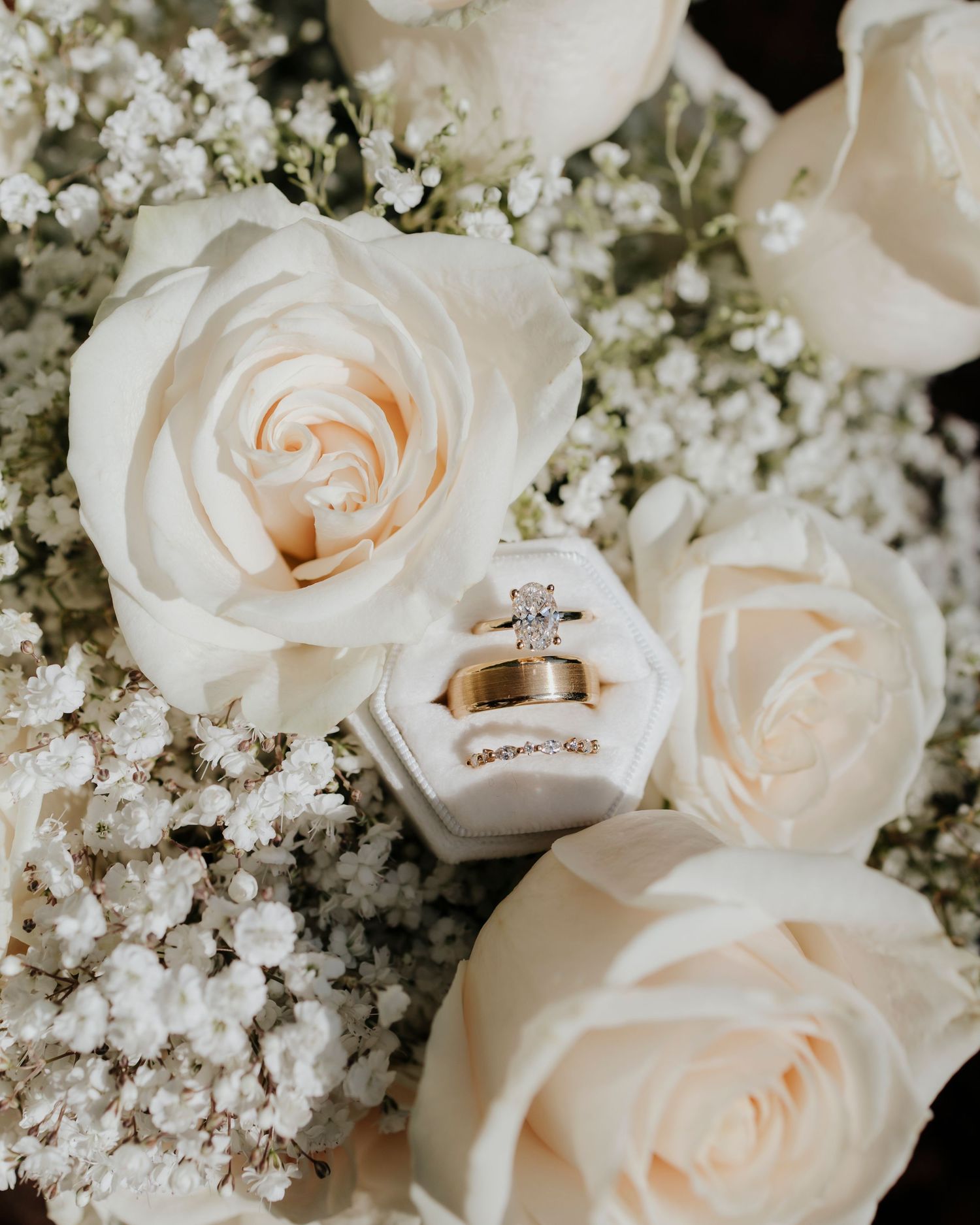 Wedding rings nestled among delicate white roses and baby's breath flowers in an elegant floral arrangement.
