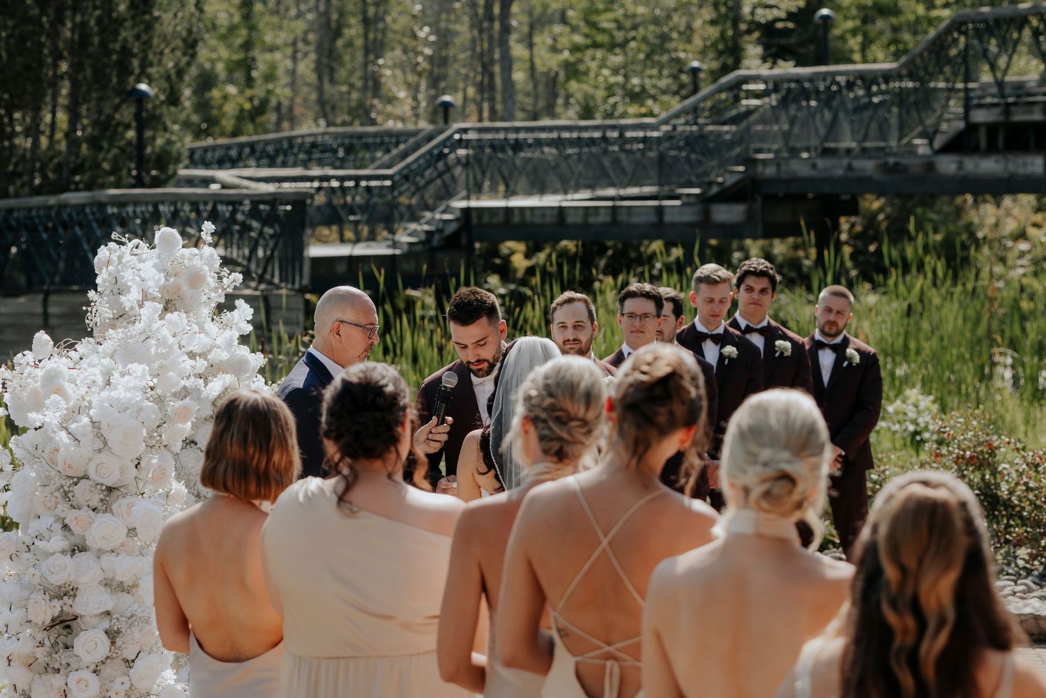 Wedding ceremony group shot with white floral arch backdrop.