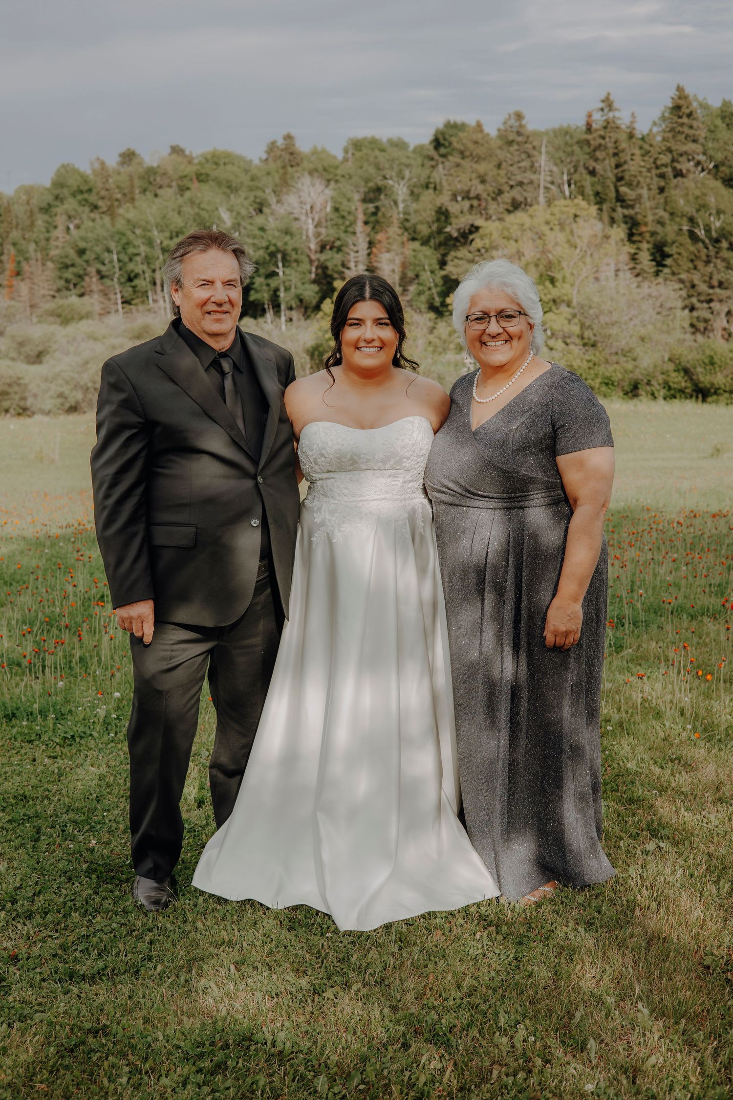 Wedding group photo outdoors with bride in white dress surrounded by loved ones.