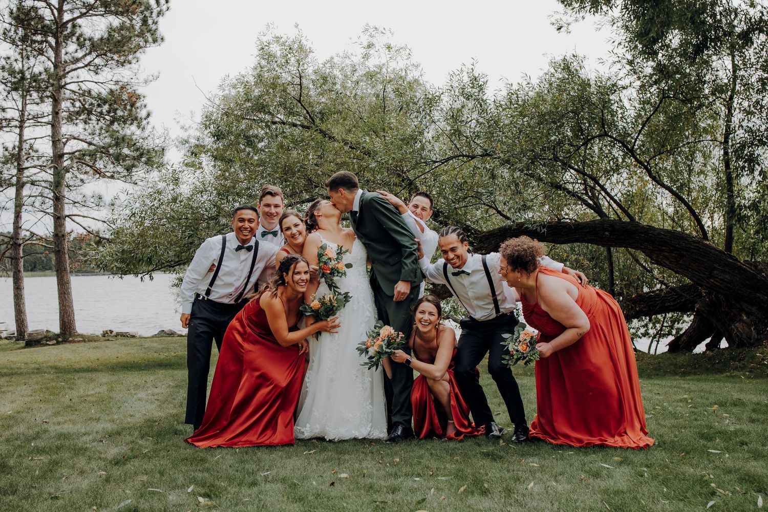 Wedding party lounges on grass for casual group photo in outdoor setting.