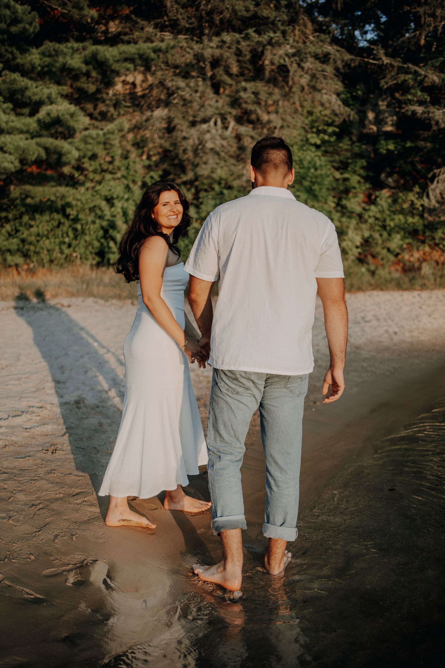 Candid shot of a couple walking barefoot on a beach during golden hour.