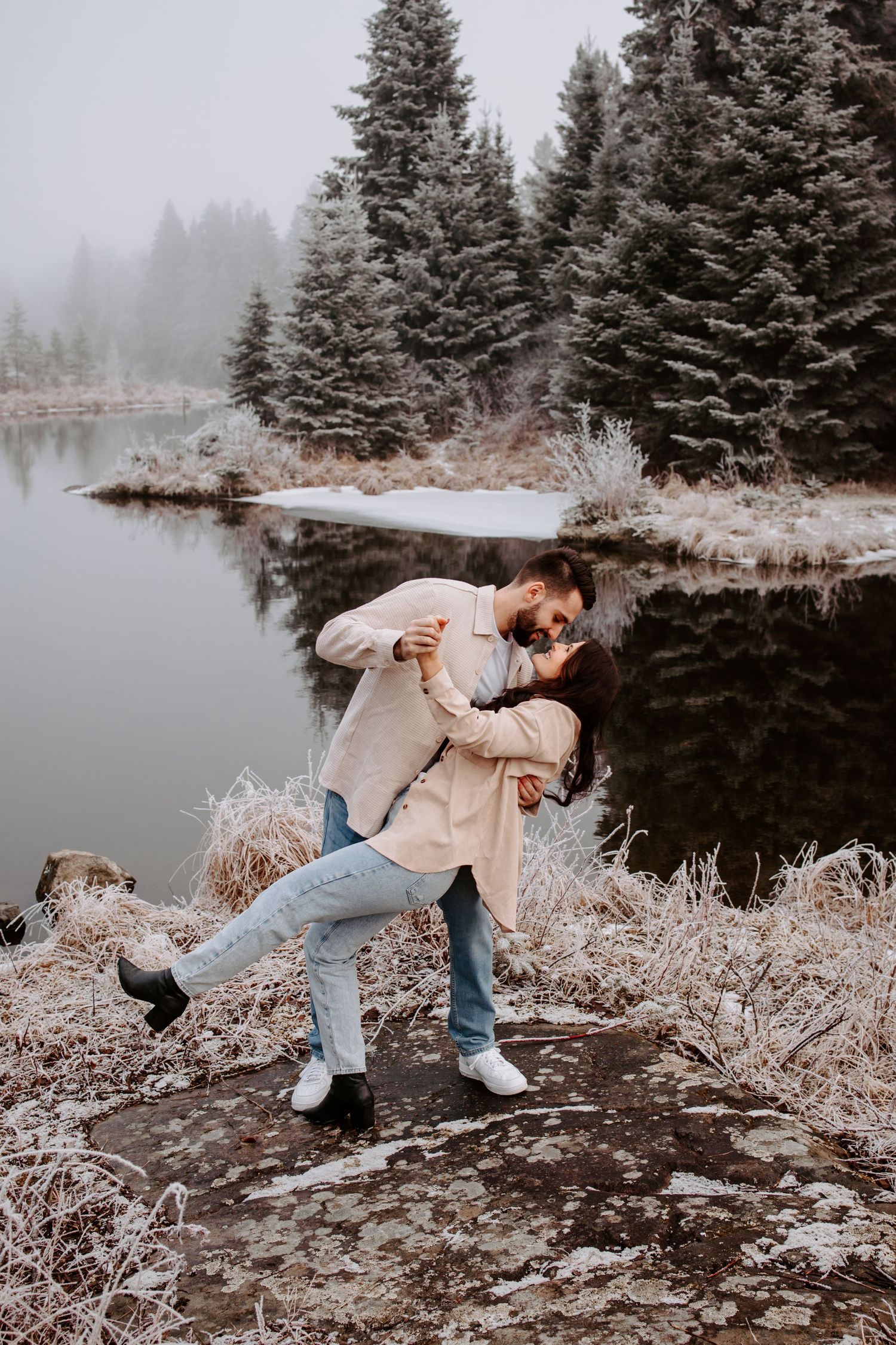 A romantic dip pose against a misty winter lake and evergreen forest backdrop.
