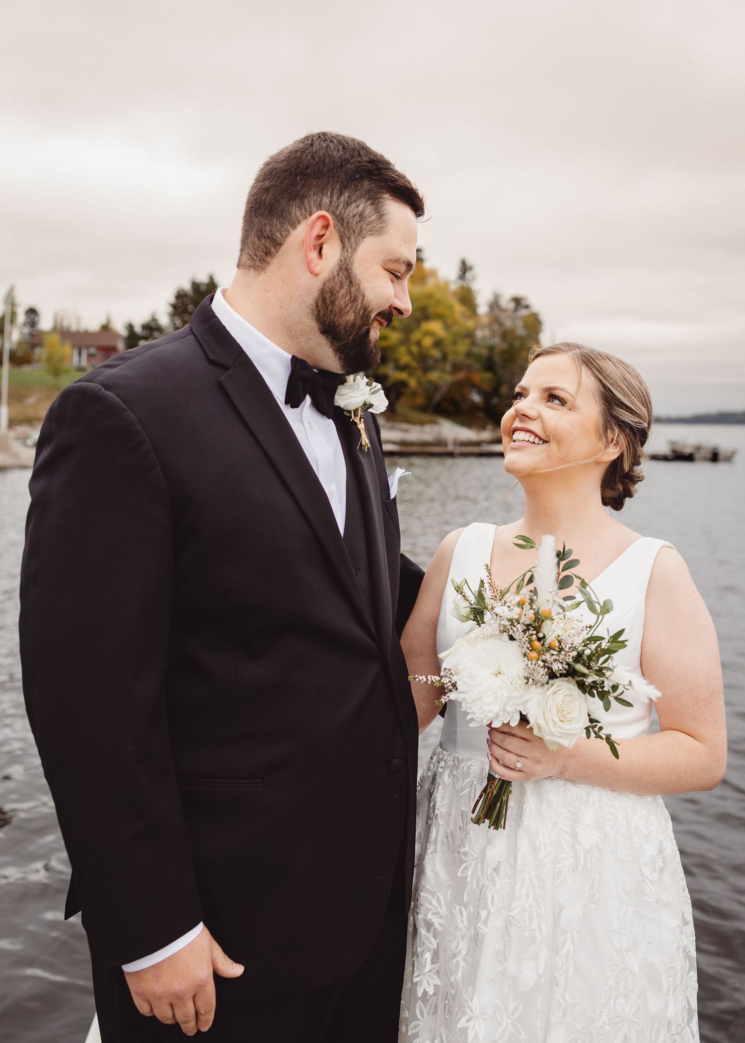 A waterfront wedding portrait captures a joyful moment between newlyweds against an autumn backdrop.
